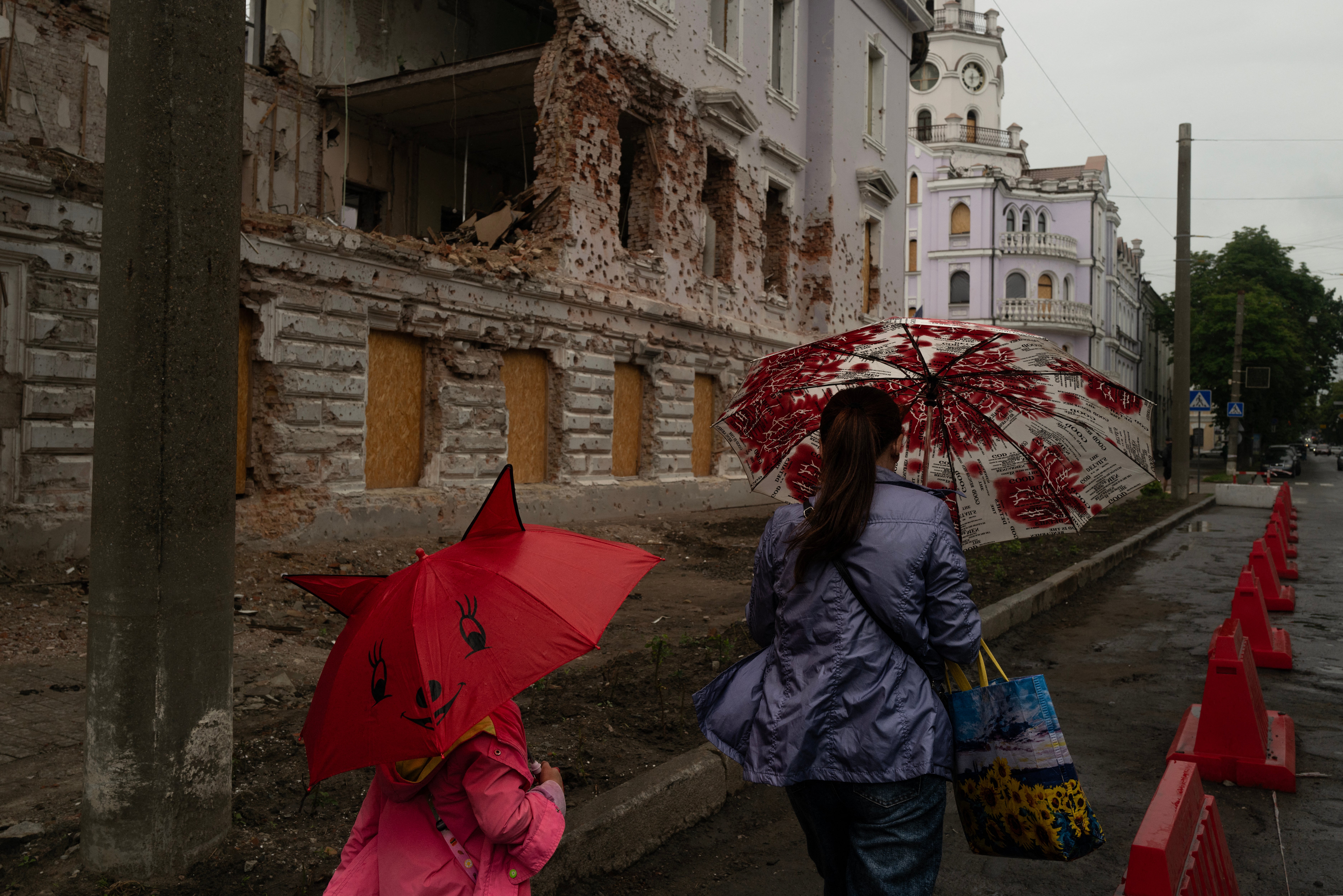A mother and daughter walk with umbrellas past a monument destroyed by Russian bombing in Sumy, north-eastern Ukraine, on June 12, 2025