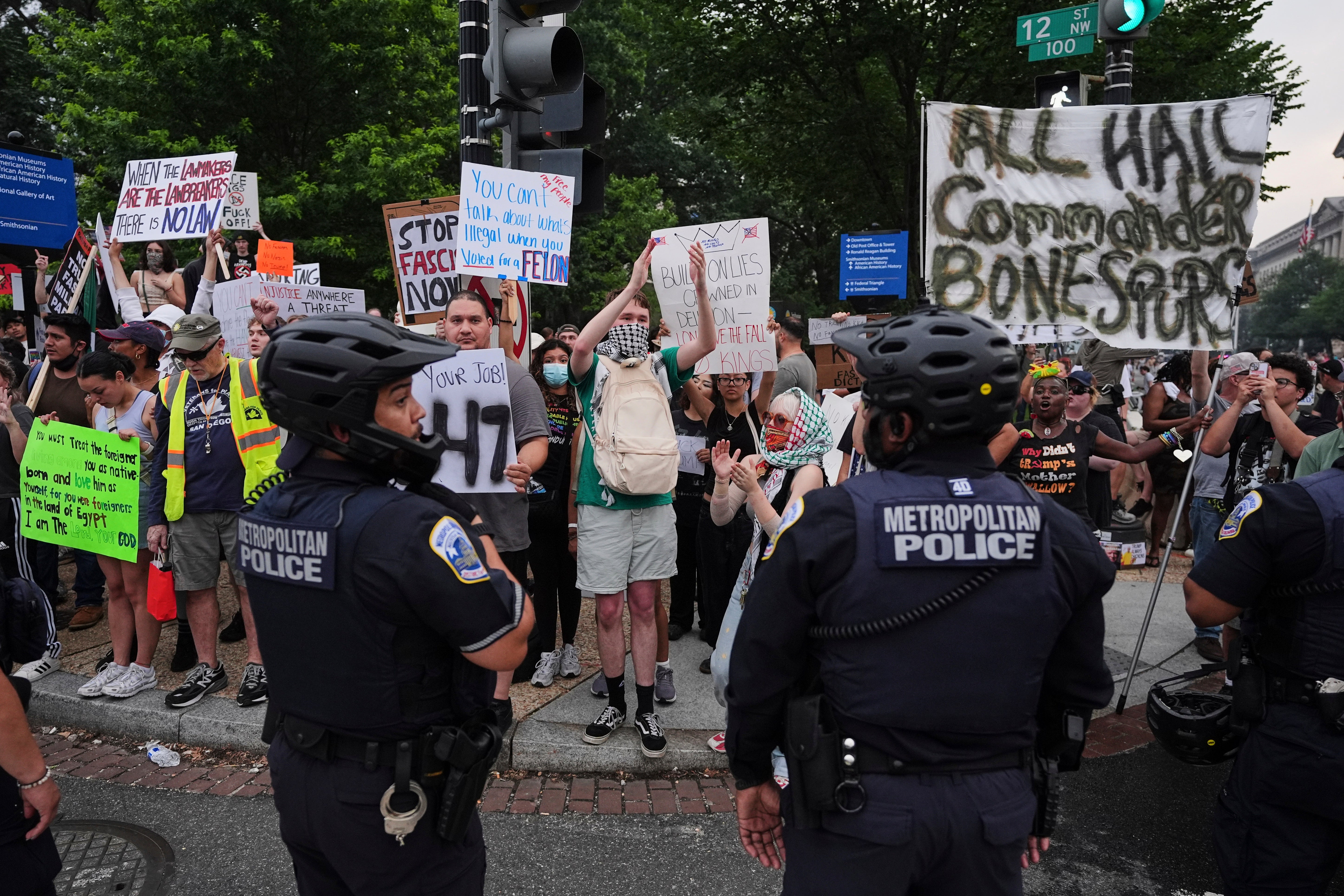 Demonstrators carry signs during a protest taking place on the day of a military parade commemorating the Army's 250th anniversary,