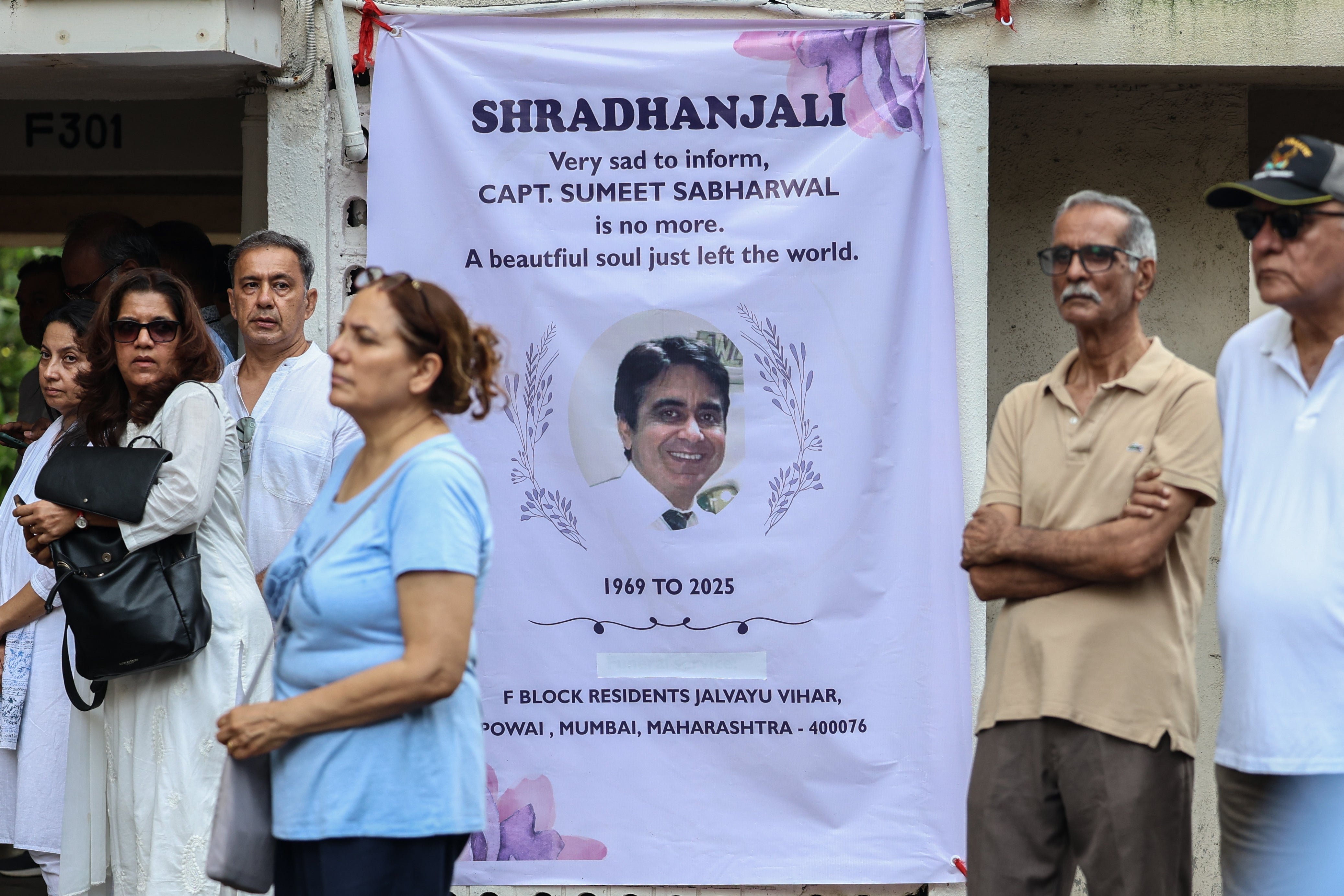 People gather near a memorial banner to pay tribute to Captain Sumeet Sabharwal, pilot of Air India flight AI171, before the funeral in Mumbai