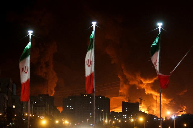 <p>Iranian flags fly as fire and smoke from an Israeli attack on Sharan Oil depot rise</p>