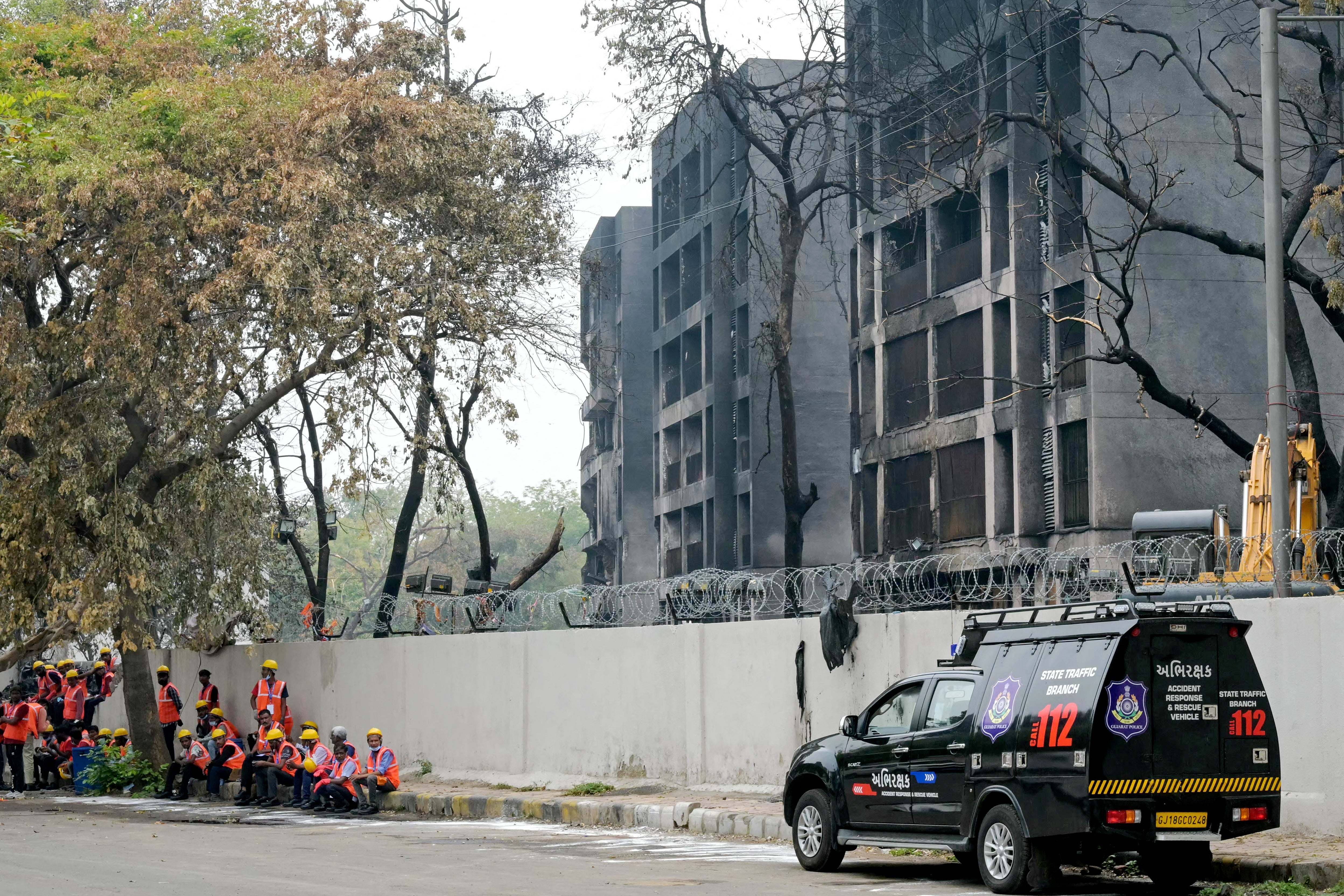 Workers wait to clear debris from the crash site of Air India flight 171, outside charred buildings at a residential area near the airport in Ahmedabad