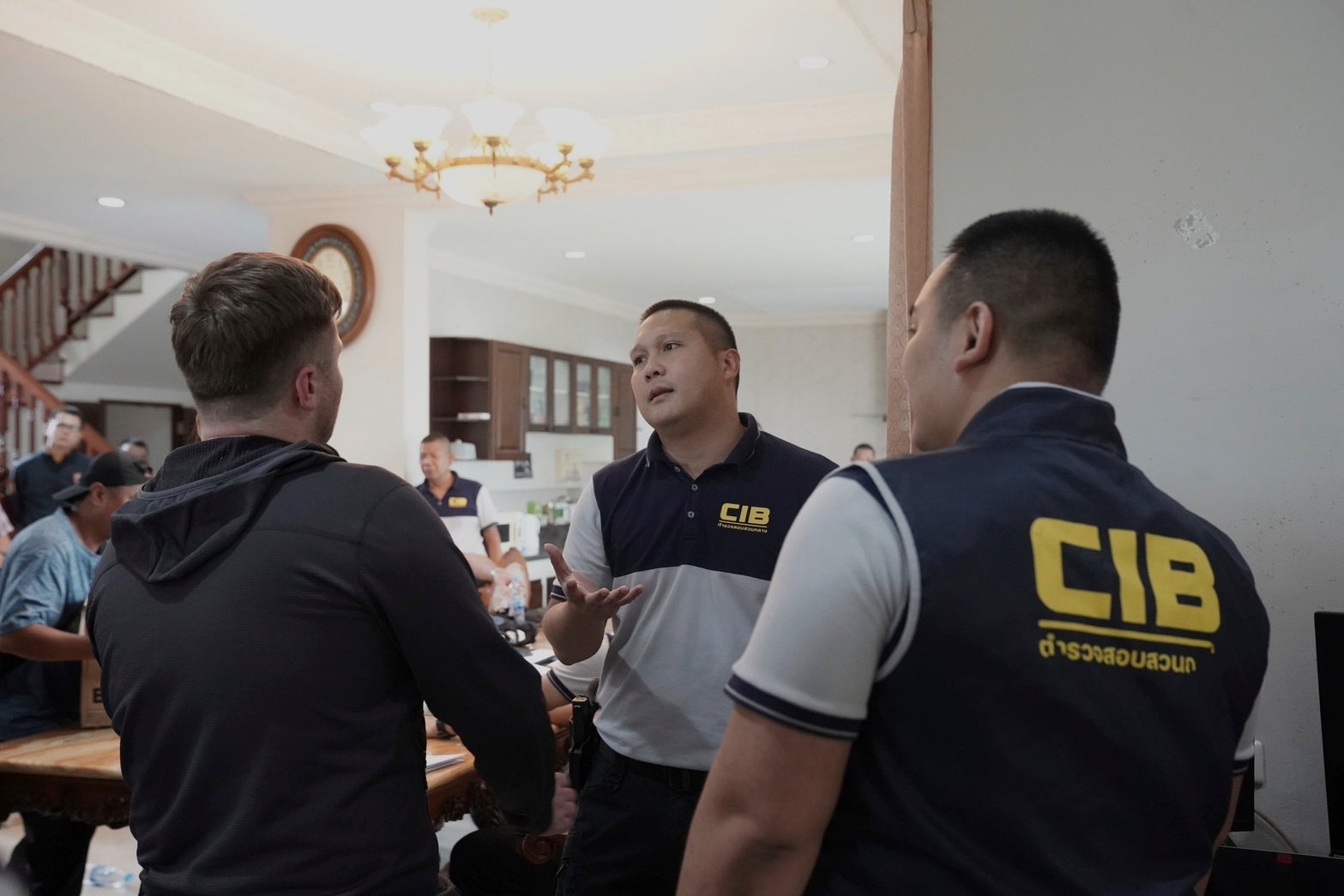 Thai Police Central Investigation Bureau personnel talk to one of the suspects, left, back to camera, at a rental house where an online investment fraud targeting Australians was allegedly being run in Samut Prakarn, Thailand.