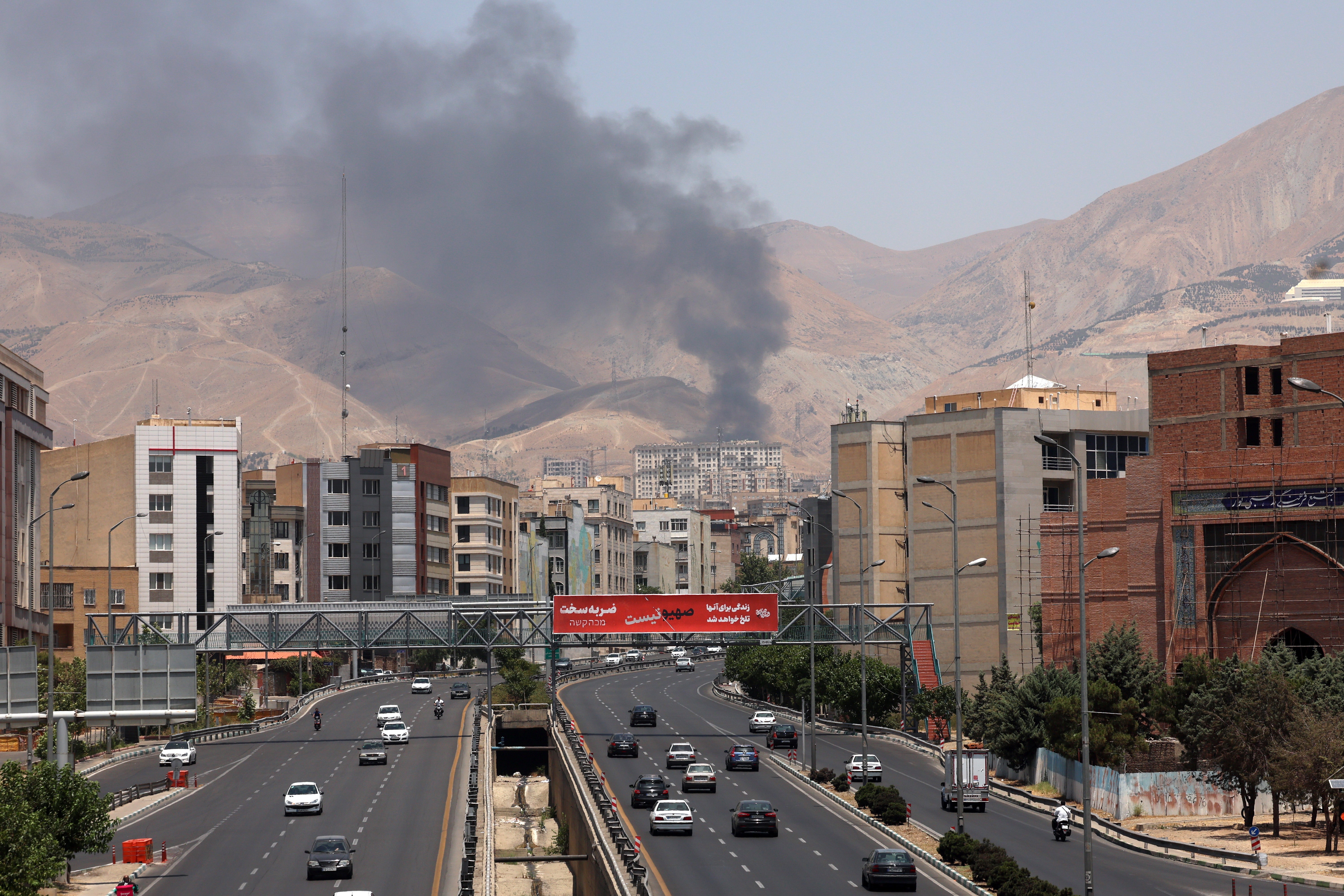 Cars drive along the motorway in Tehran as smoke billows following an Israeli missile attack