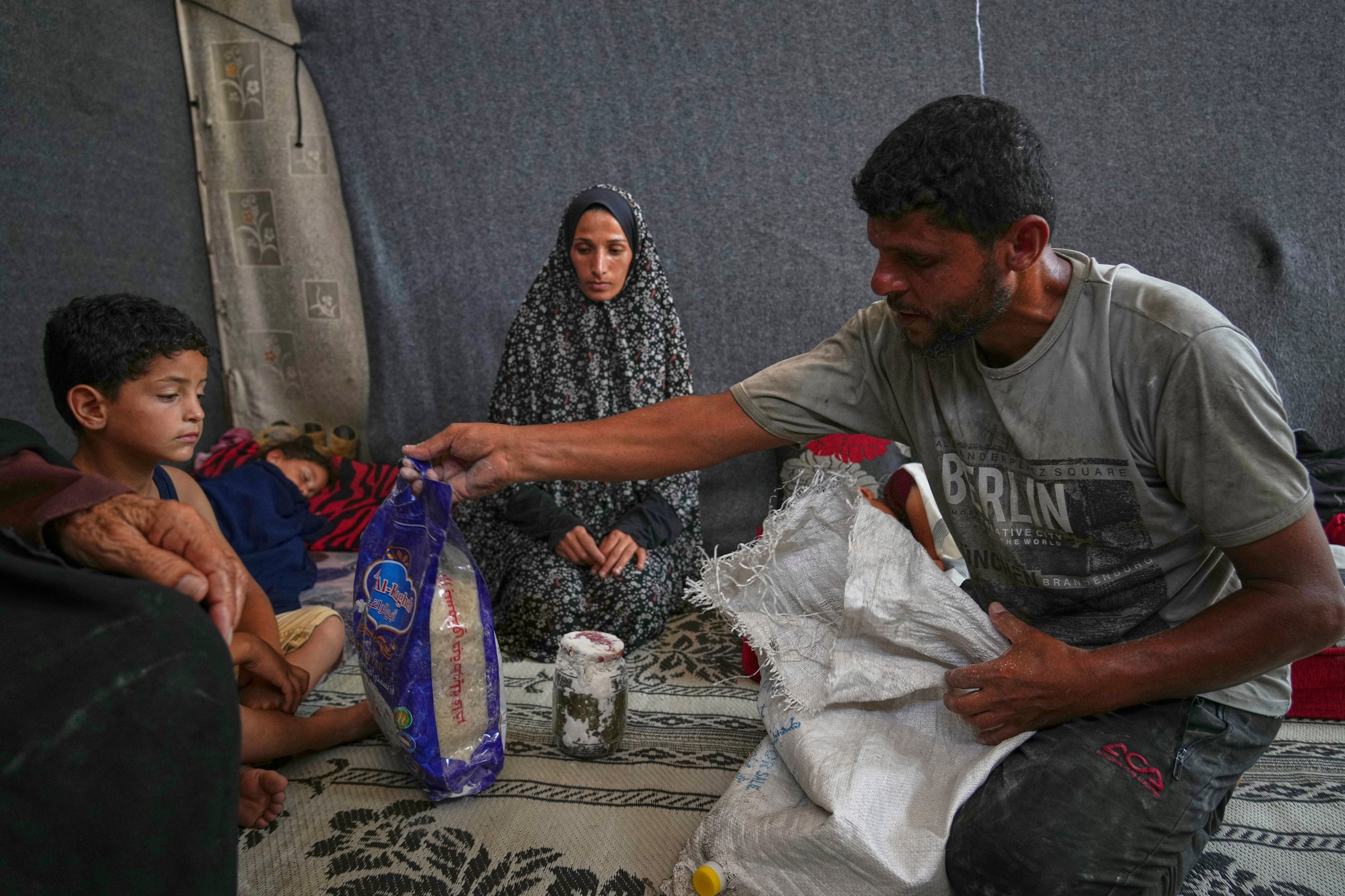 Omar al-Hobi, 43, from Rafah, unpacks a bag of food he collected at a distribution center run by the Gaza Humanitarian Foundation in the southern Gaza Strip, as he arrives at his family's tent in Khan Younis, Tuesday, June 10, 2025. At left are his children and his wife, Anwaar Saleh.