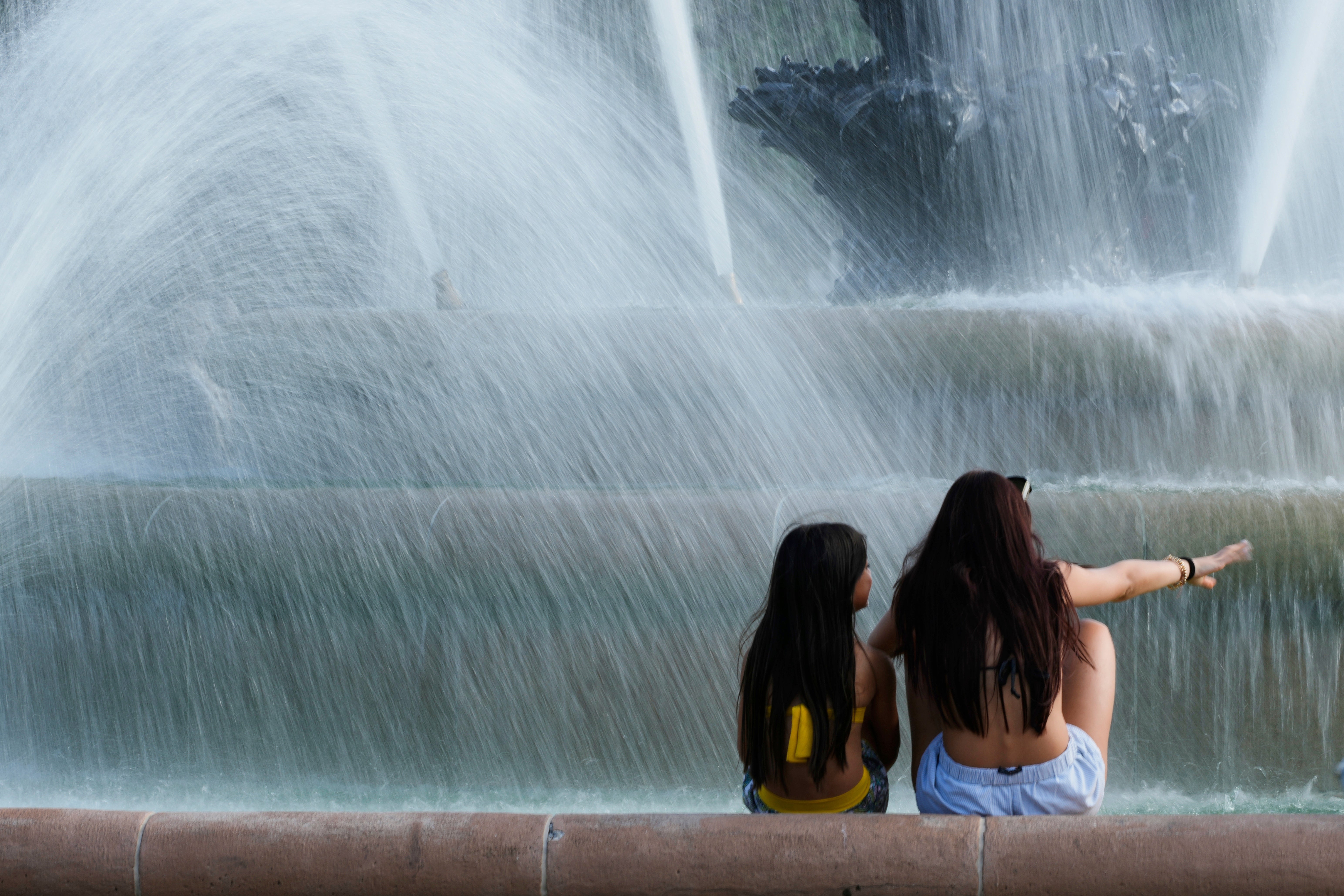 Kids cool off in the mist from a fountain as temperatures approach 100 degrees, Friday, June 20, 2025, in Kansas City, Mo.