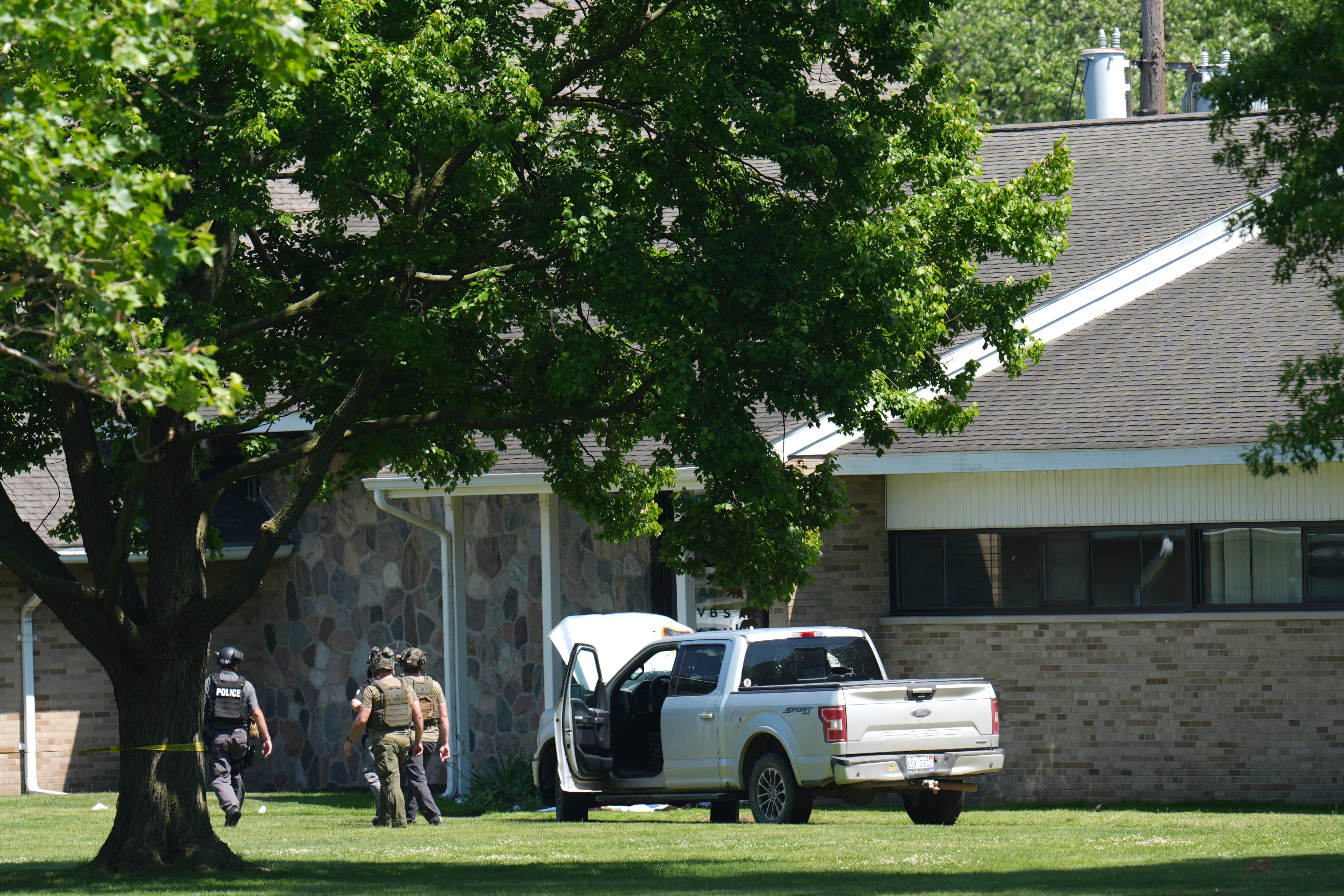 Police walk by an idle vehicle near CrossPointe Community Church in Wayne, Michigan, on Sunday, June 22, 2025