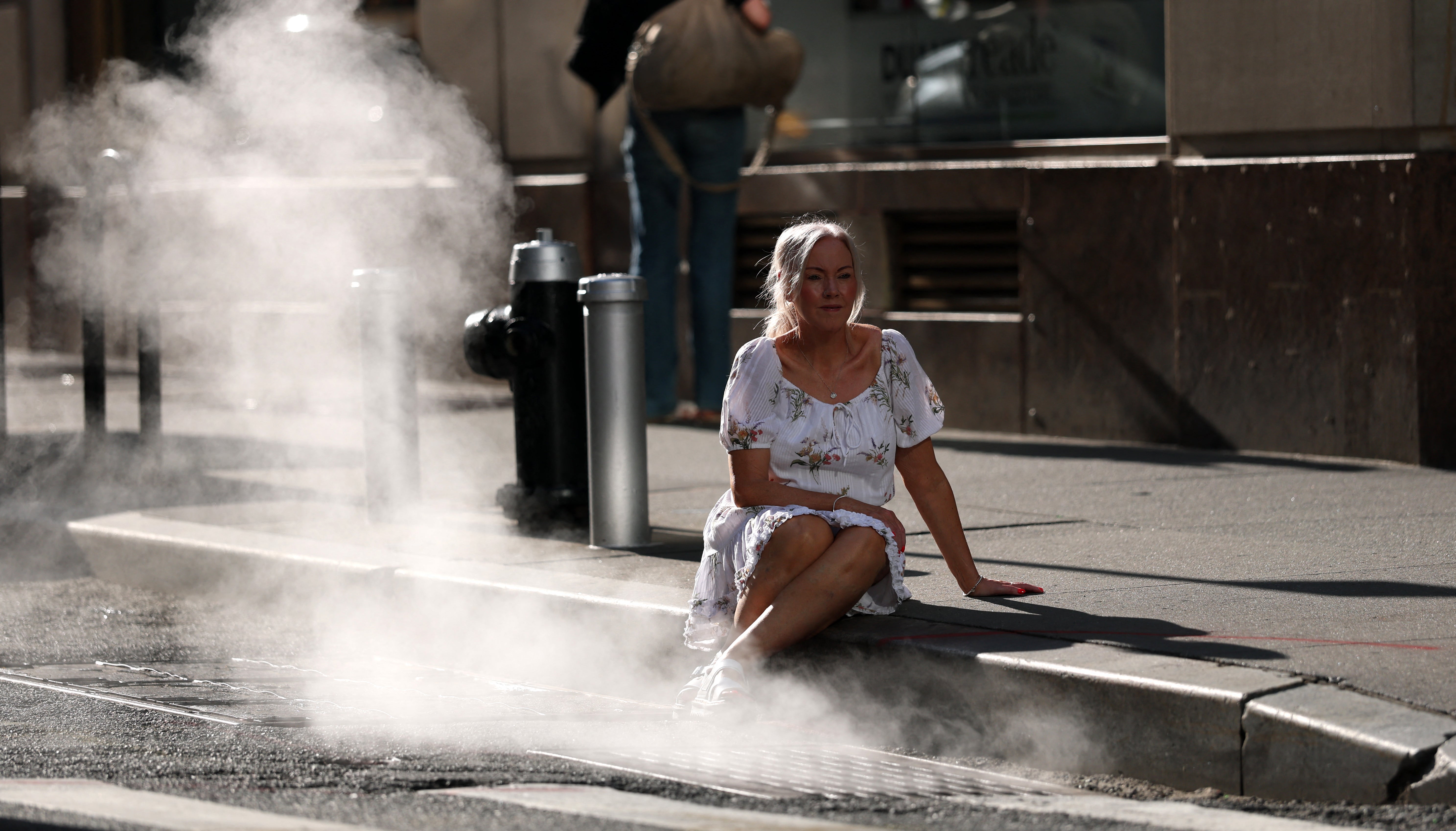 A tourist in New York City poses on Monday near hot steam on one of the hottest days of the year thus far. New York was under a state of emergency