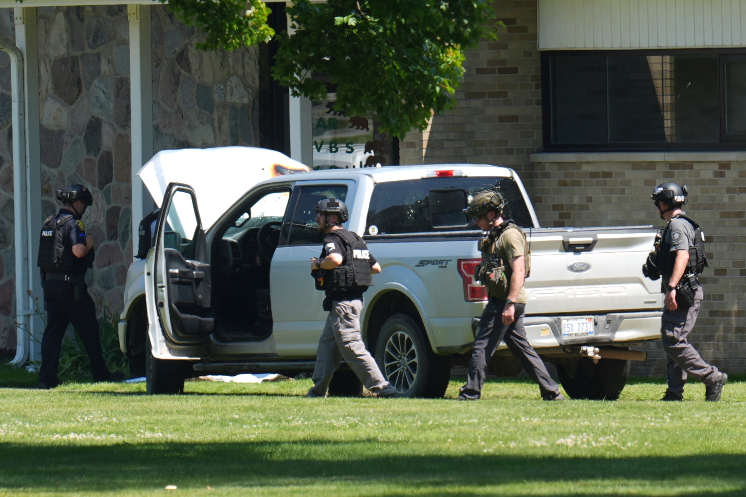 Police walk by a vehicle that ran down an alleged gunman, preventing a mass shooting at a suburban Detroit church on Sunday, June 22, 2025