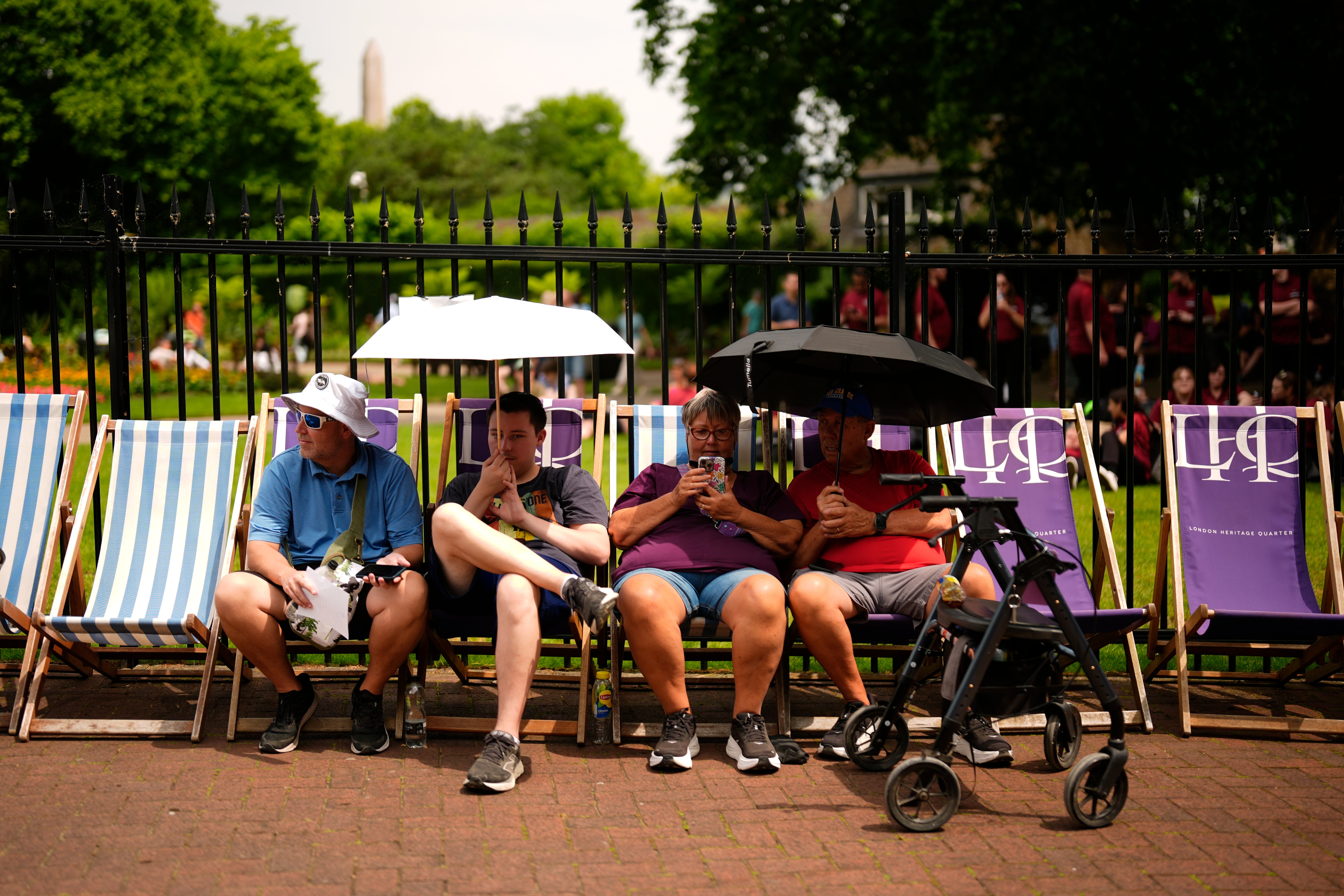 People shield from the sun under umbrellas in Victoria Embankment Gardens, London
