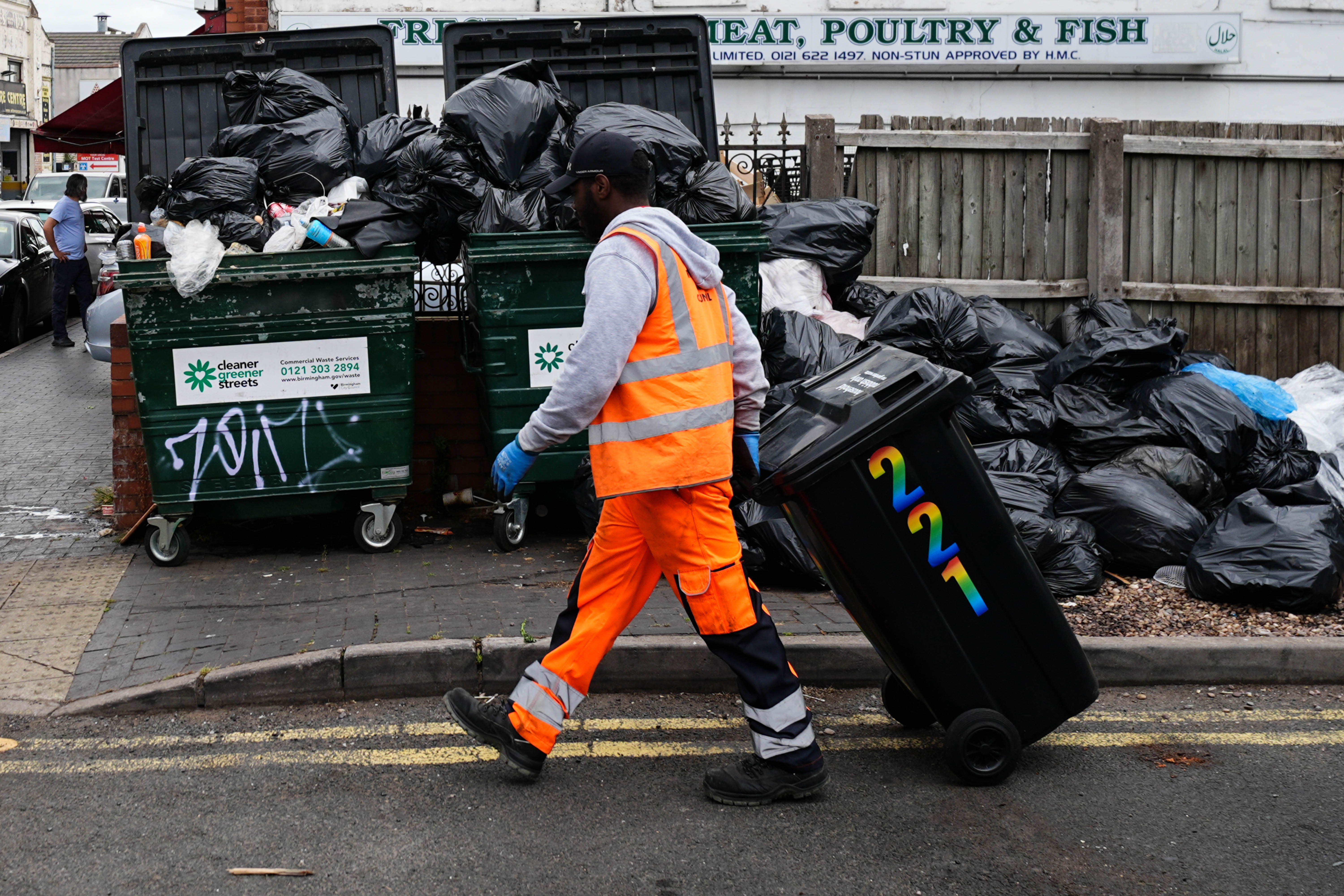 A refuse worker collects a bin by uncollected waste bags in the Aston area of Birmingham