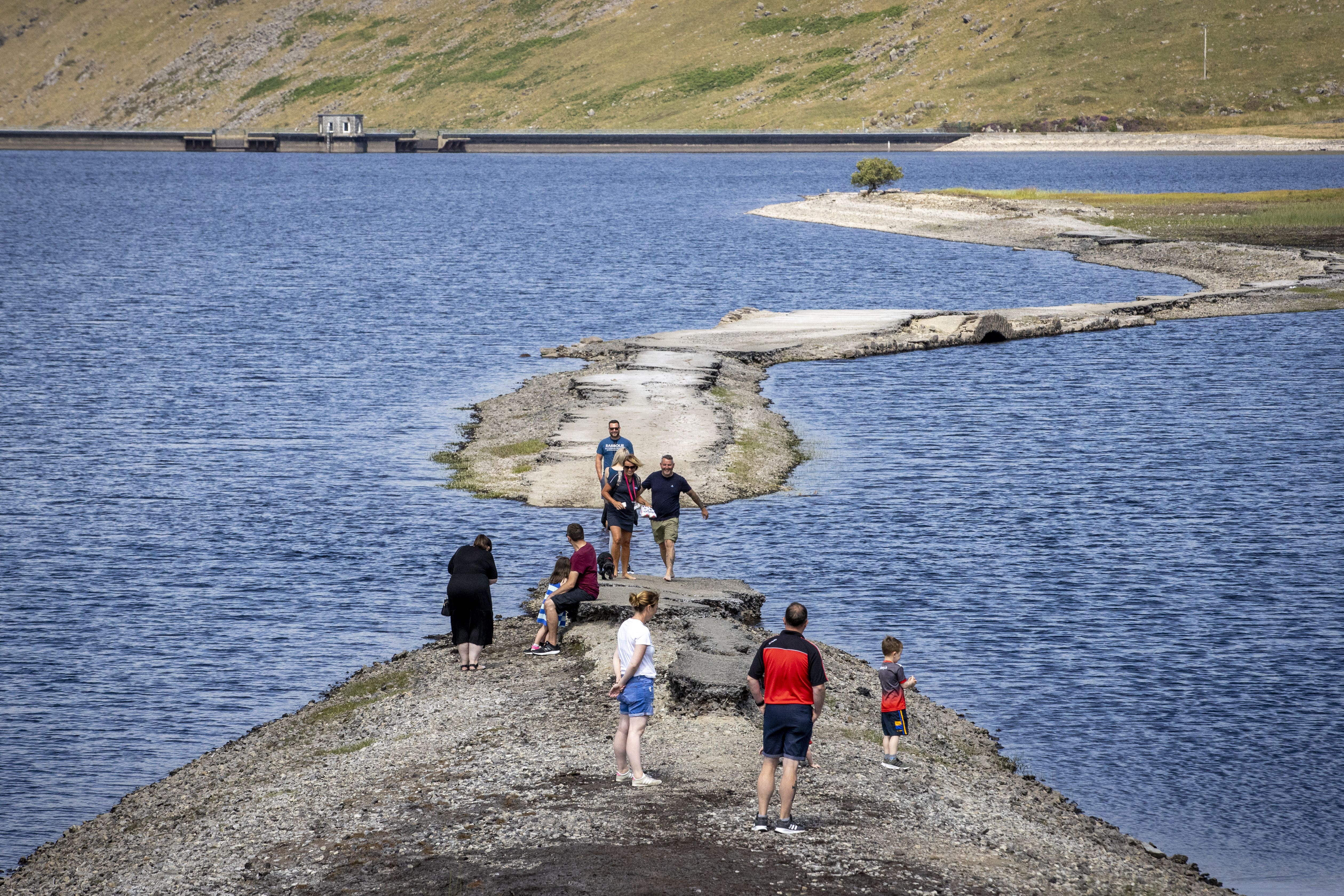 People walking along a pathway exposed by the falling water level at Spelga Reservoir (PA)