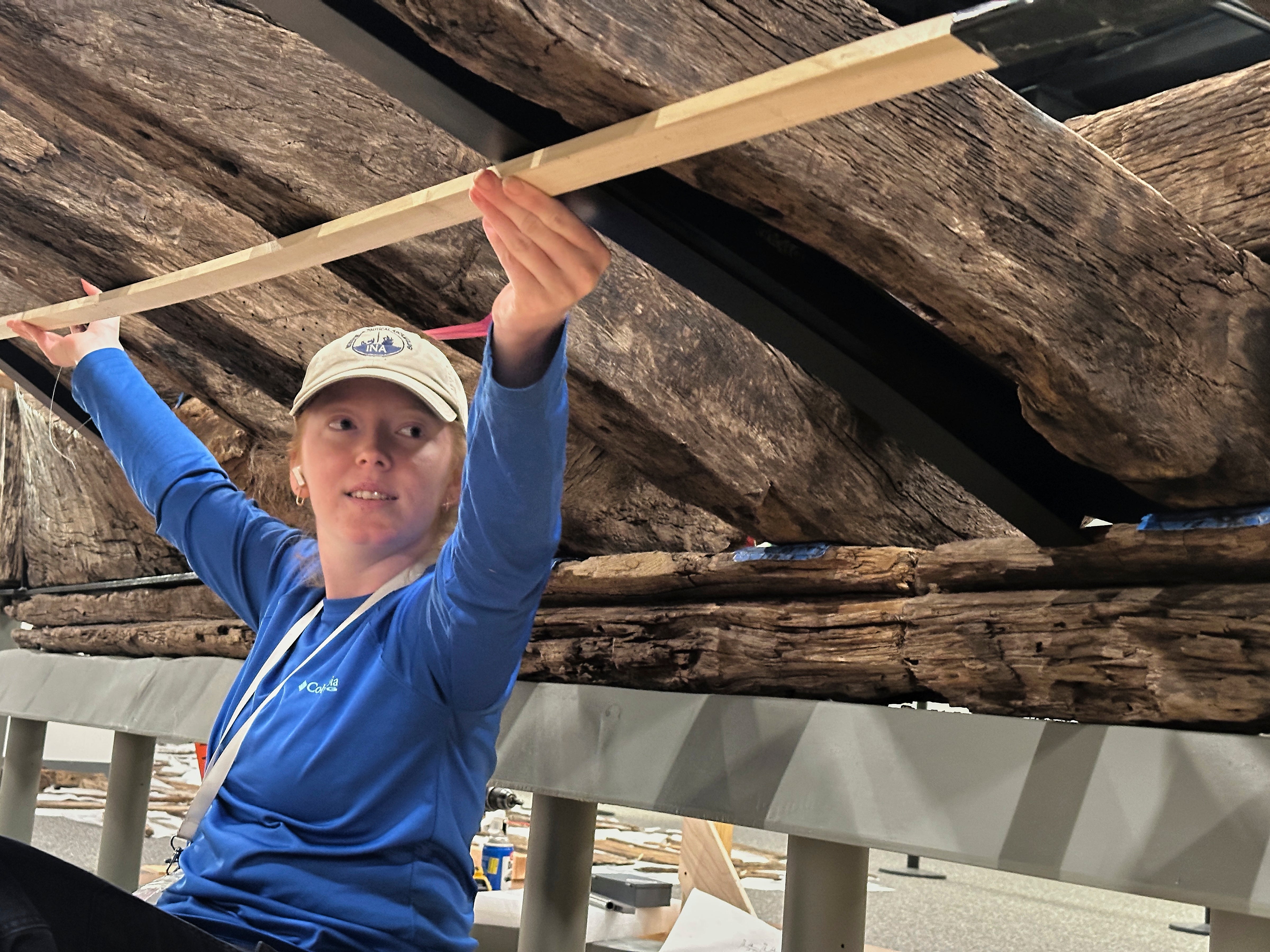 Research assistant Alyssa Carpenter works beneath a wooden Revolutionary War-era gunboat to prepare for the craft's partial reconstruction at the New York State Museum