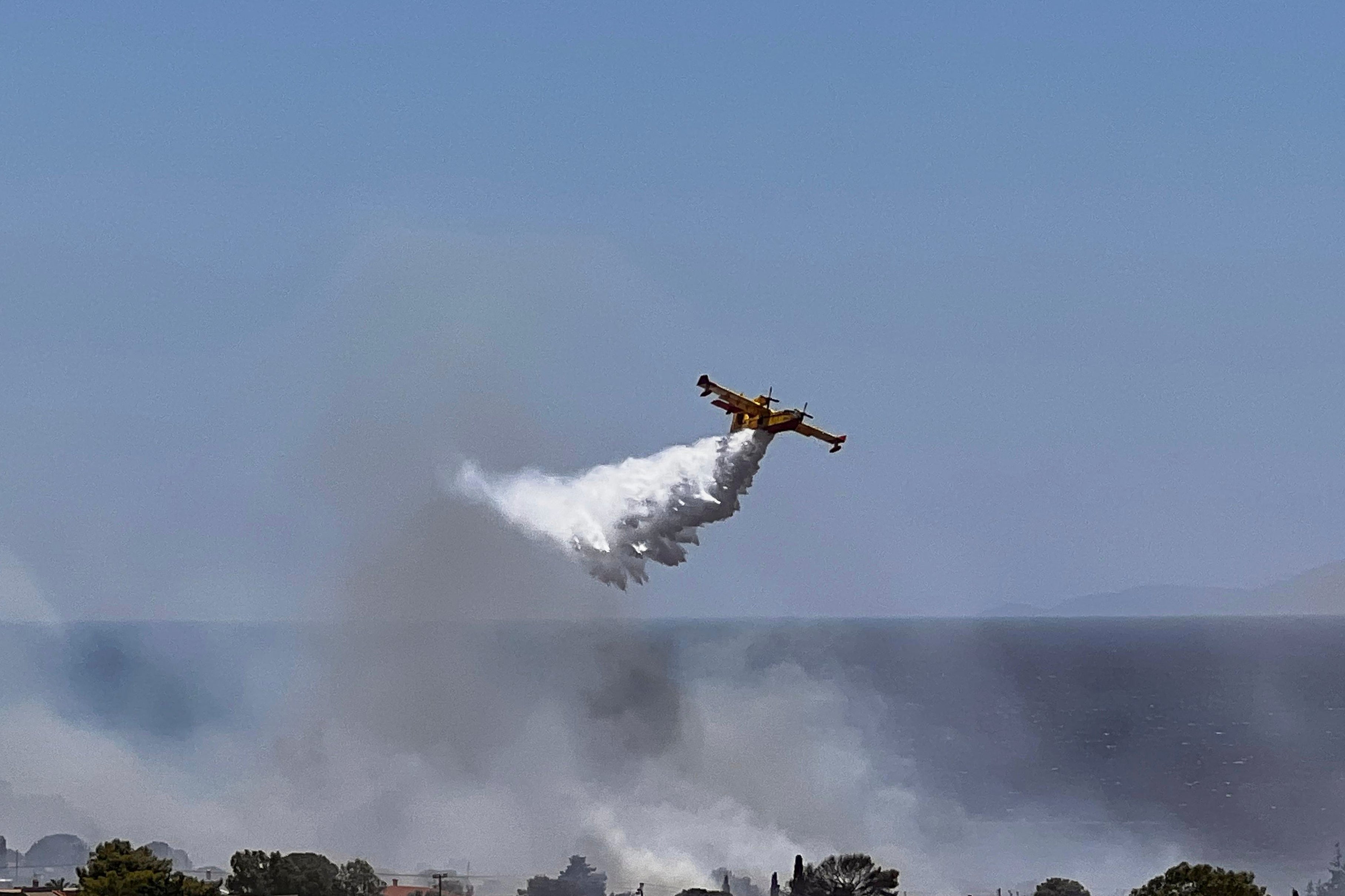 A Firefighting plane drops water while battling a blaze in the seaside area of Palaia Fokaia, south of Athens, Thursday, June 26, 2025, as authorities evacuate five locations during Greece's first summer heatwave with temperatures nearing 40 degrees Celsius (104 Fahrenheit).(AP Photo/Giorgos Delveroudis)
