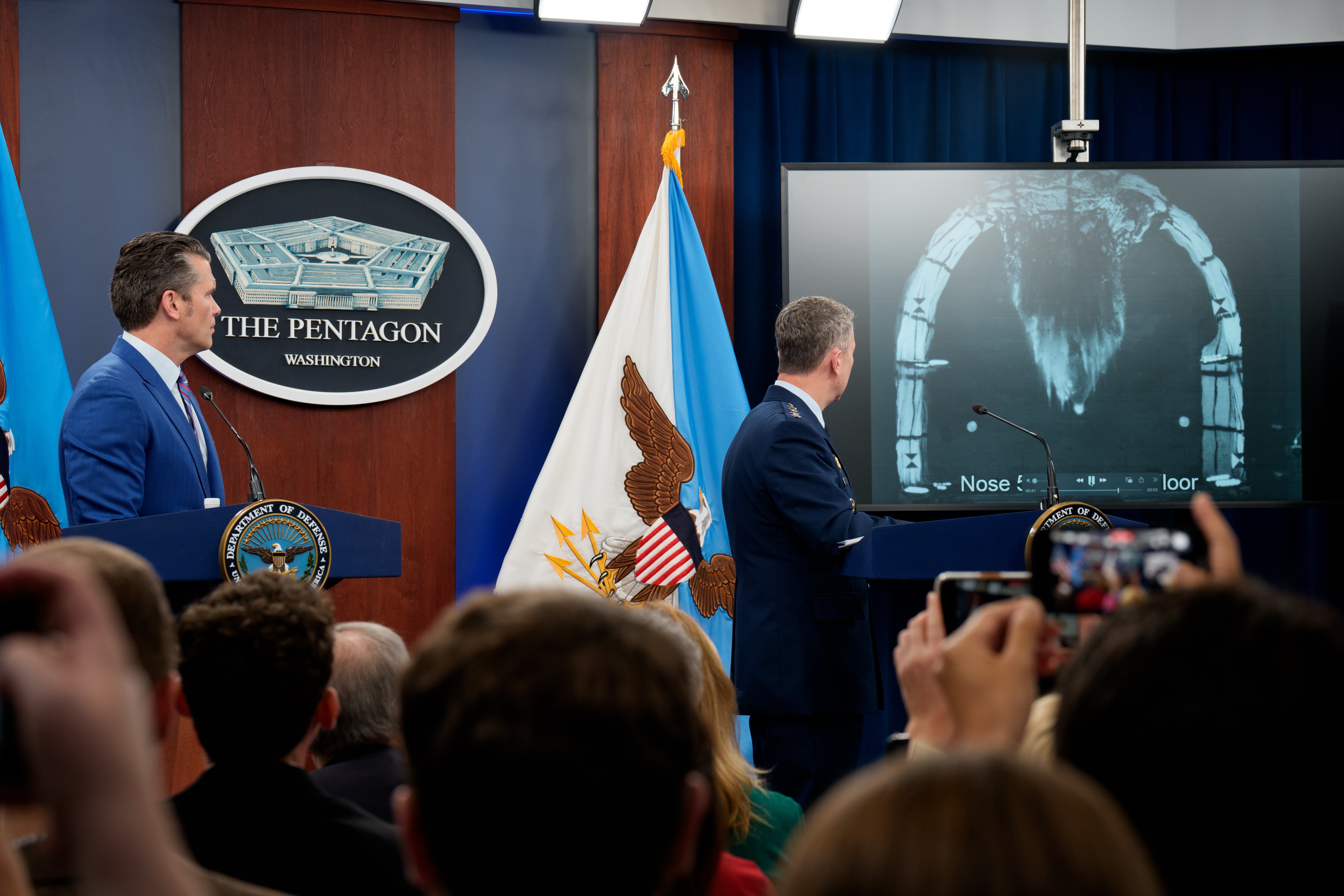 Defense Secretary Pete Hegseth (L) and Chairman of the Joint Chiefs of Staff Air Force Gen. Dan Caine (R) watch a video of a bombing test of the Massive Ordnance Penetrator used in the attack on the Iranian Fordow Fuel Enrichment Plant.