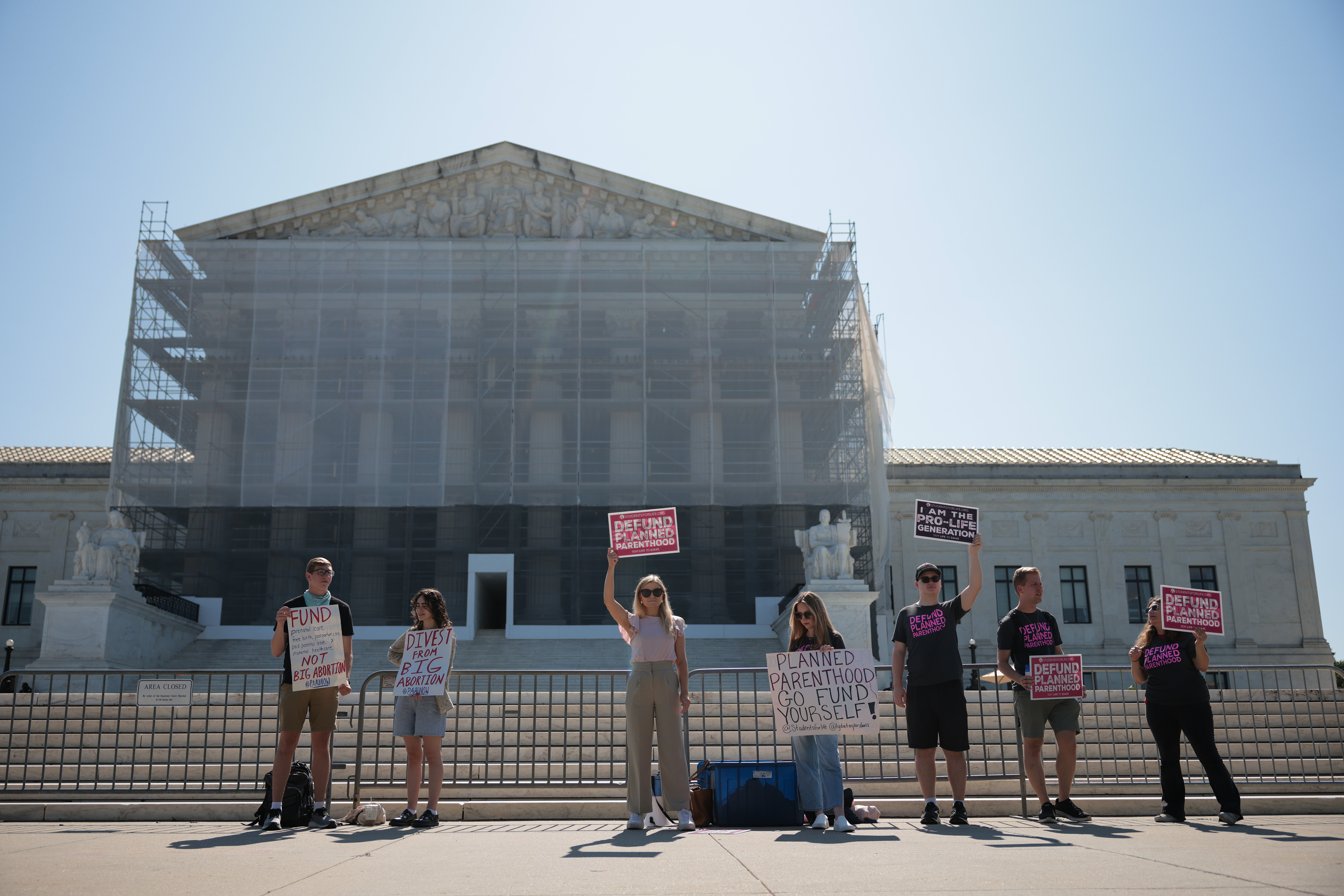Protestors holding ‘Defund Planned Parenthood’ signs stand outside of the Supreme Court