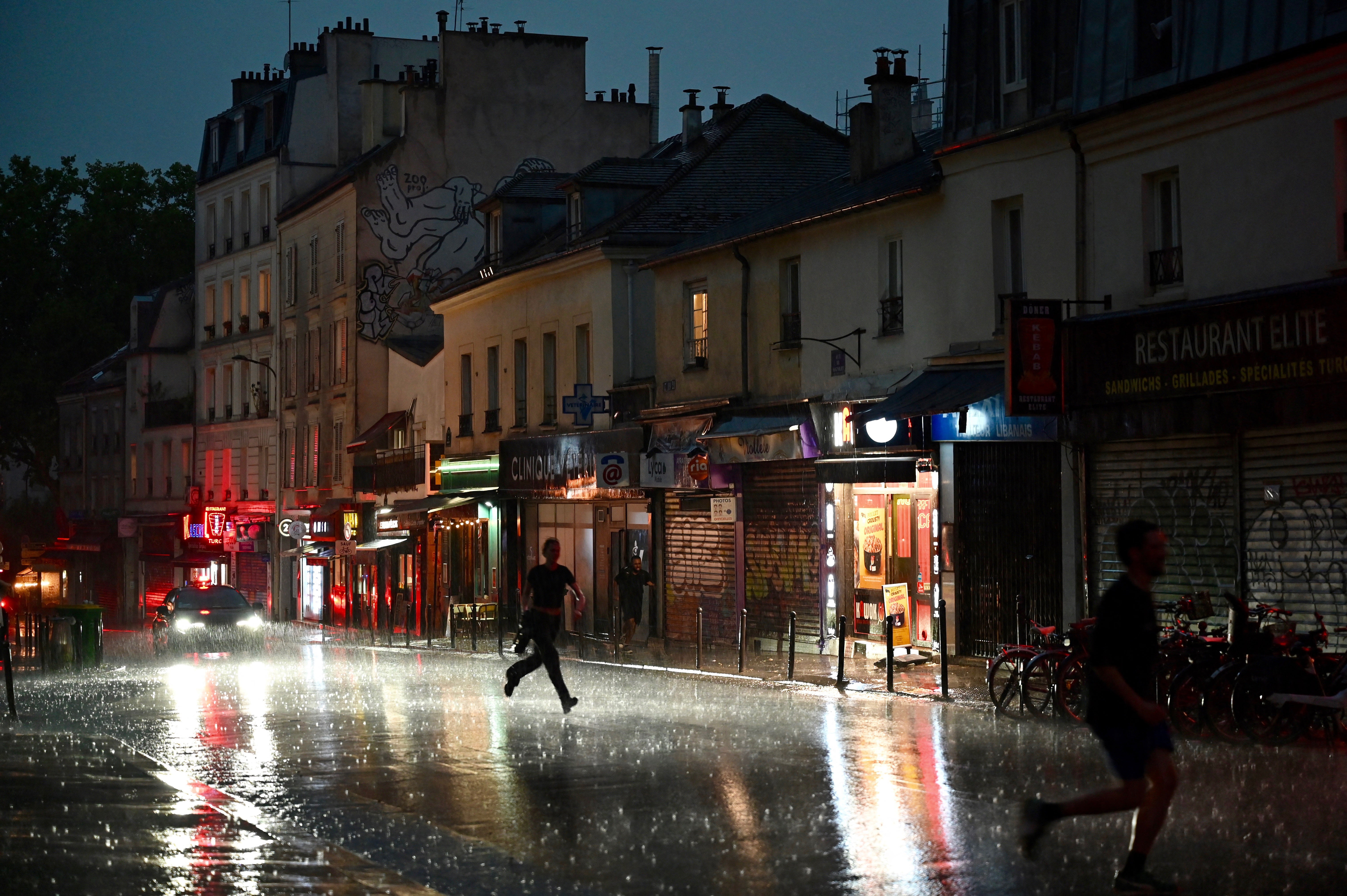People run for shelter on a street in the 20th Arrondissement during a thunderstorm, in Paris, on June 25, 2025. (Photo by Christophe DELATTRE / AFP) (Photo by CHRISTOPHE DELATTRE/AFP via Getty Images)