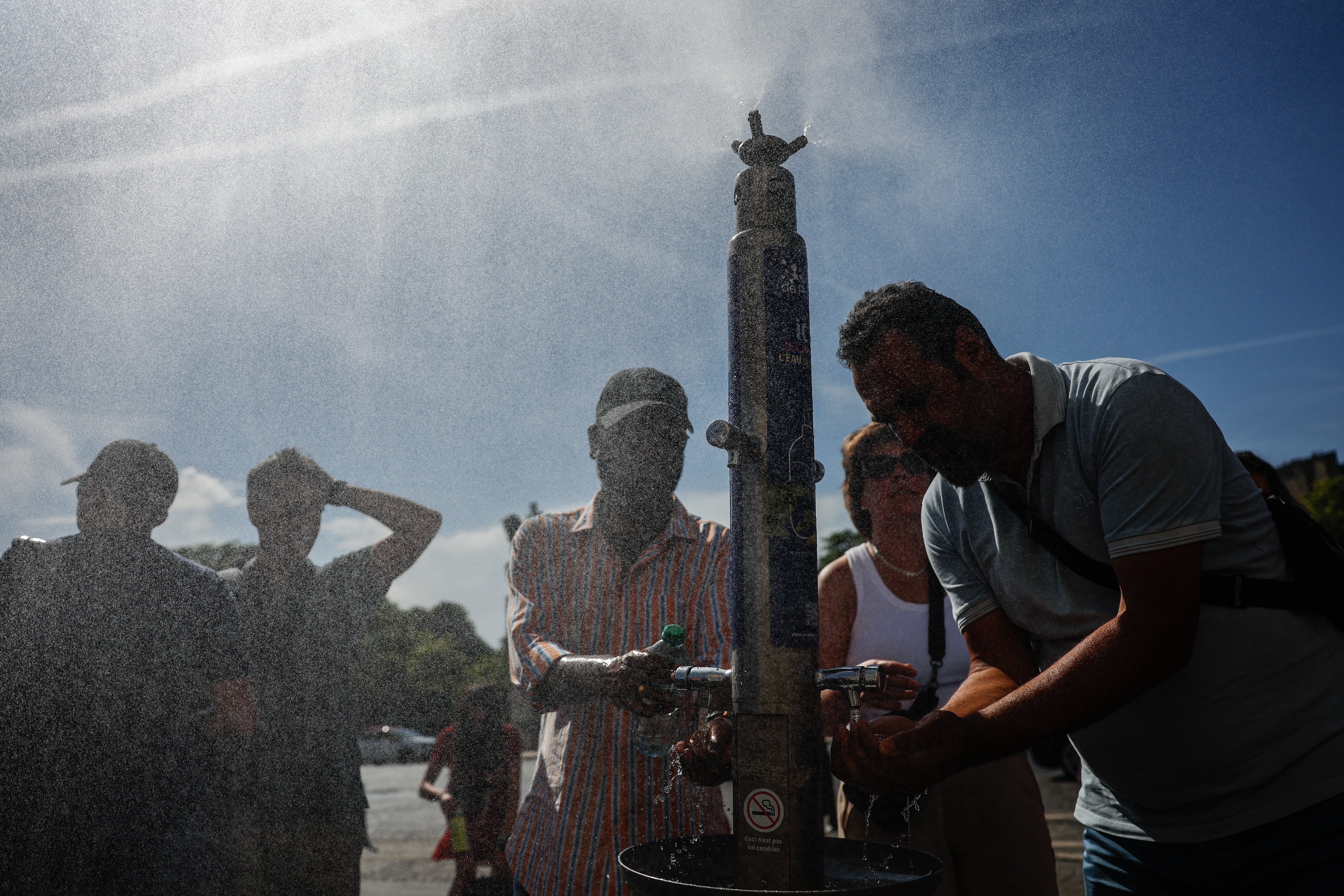 People cool down at a water fountain during a heatwave in Paris