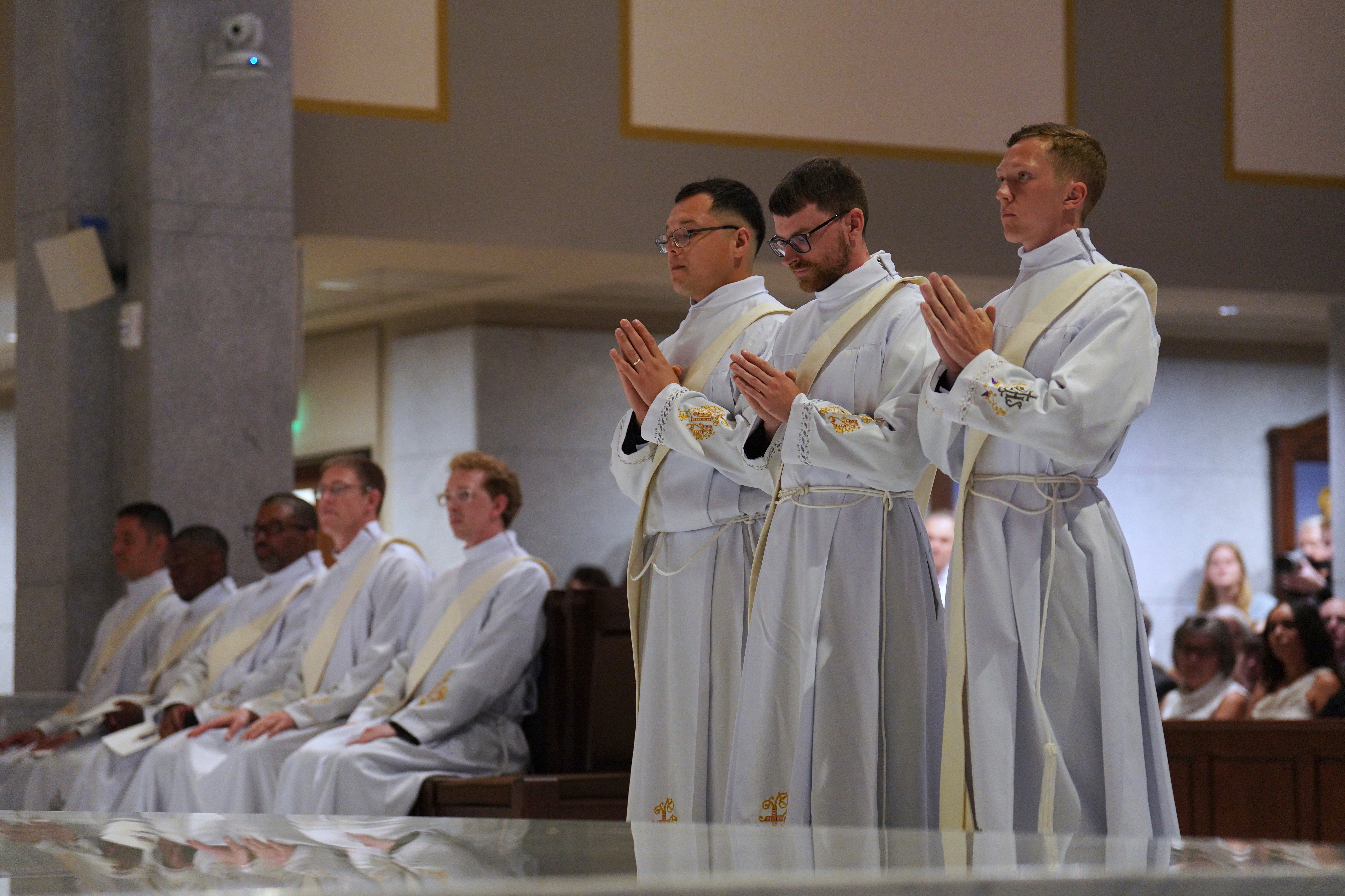 Deacons Emmanuel Carreno Garcia, left, Tim Banach, center, and Joseph Connor, right, stand as all 12 names soon to join the priesthood are called during an ordination Mass at the Cathedral of Saint Thomas More in Arlington