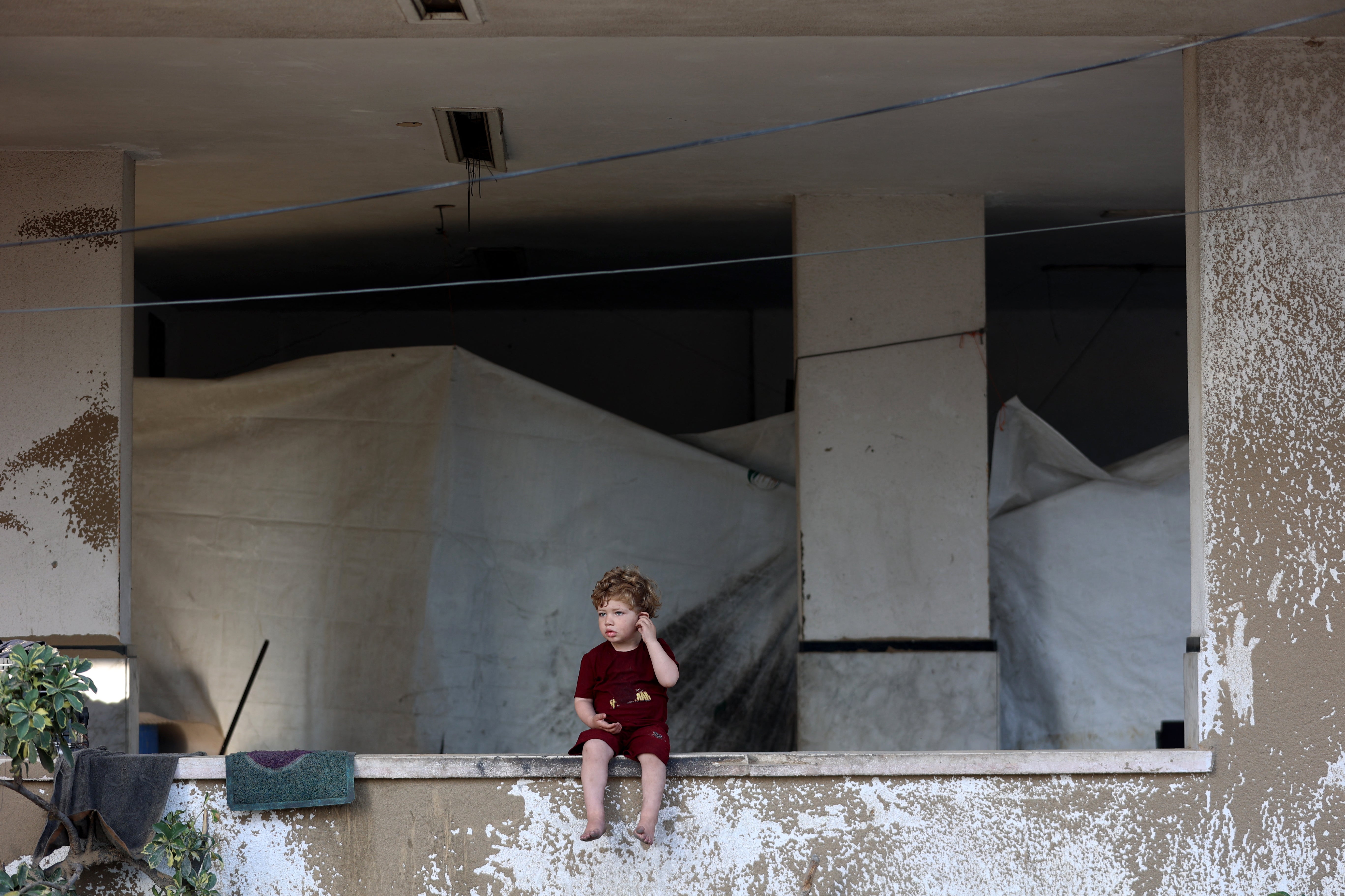 A tarpaulin shelter is setup under a building as a Palestinian child sits on a ledge after the Israeli army targeted the tents of displaced people