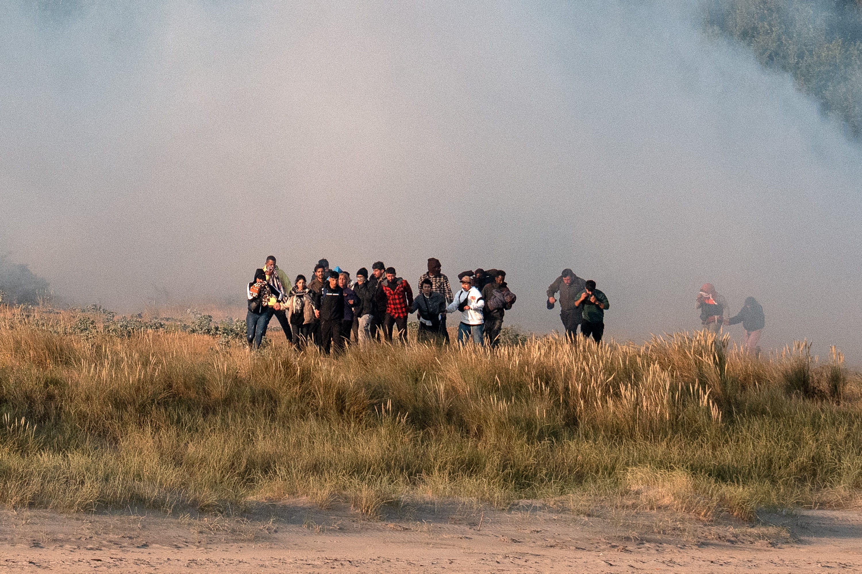 Migrants walk through a cloud of tear gas fired by police as they try and board dinghies to sail into the English Channel on June 17, 2025 in Gravelines, France.