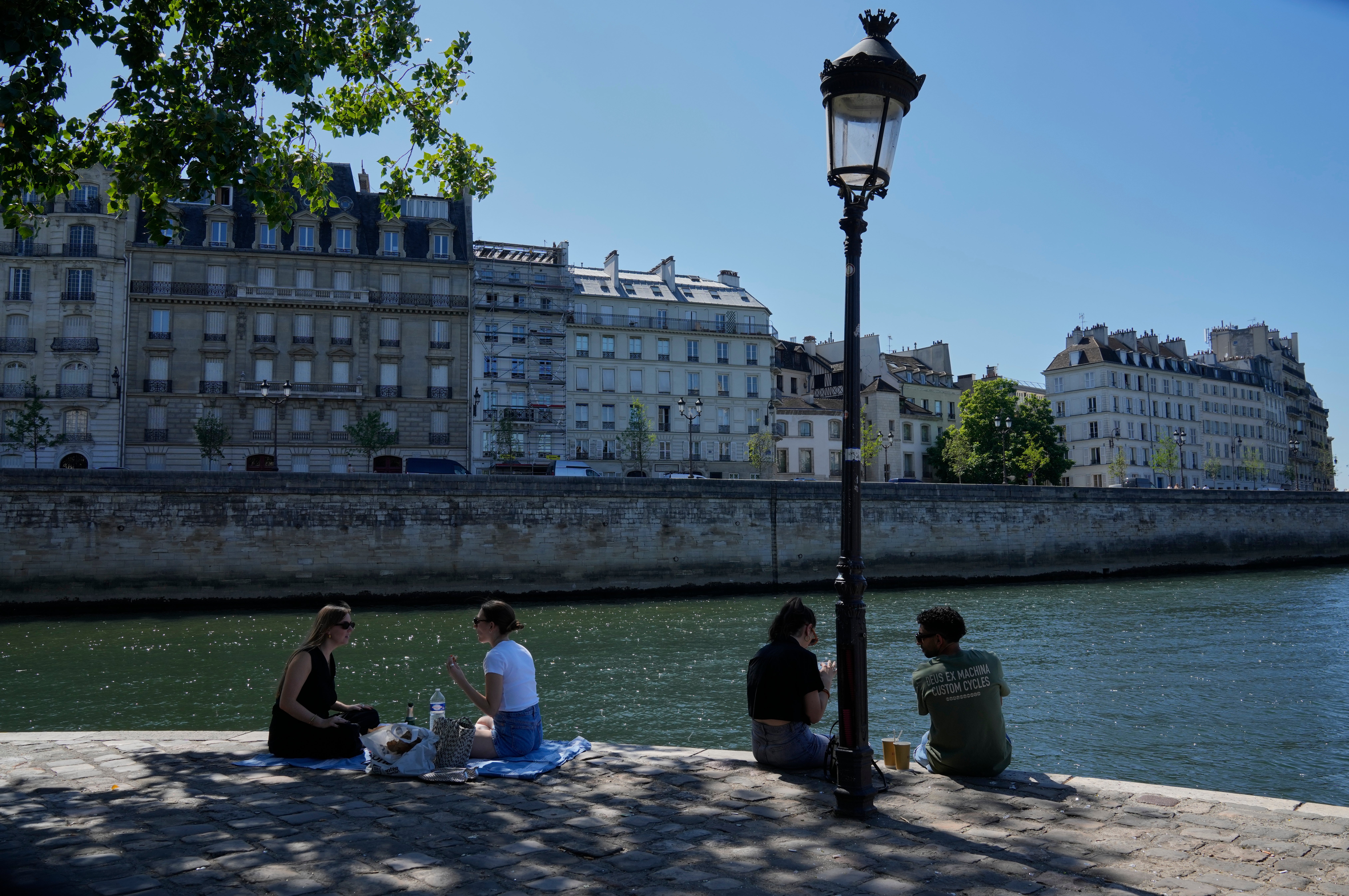 People sit in the shade along the Seine river in Paris.