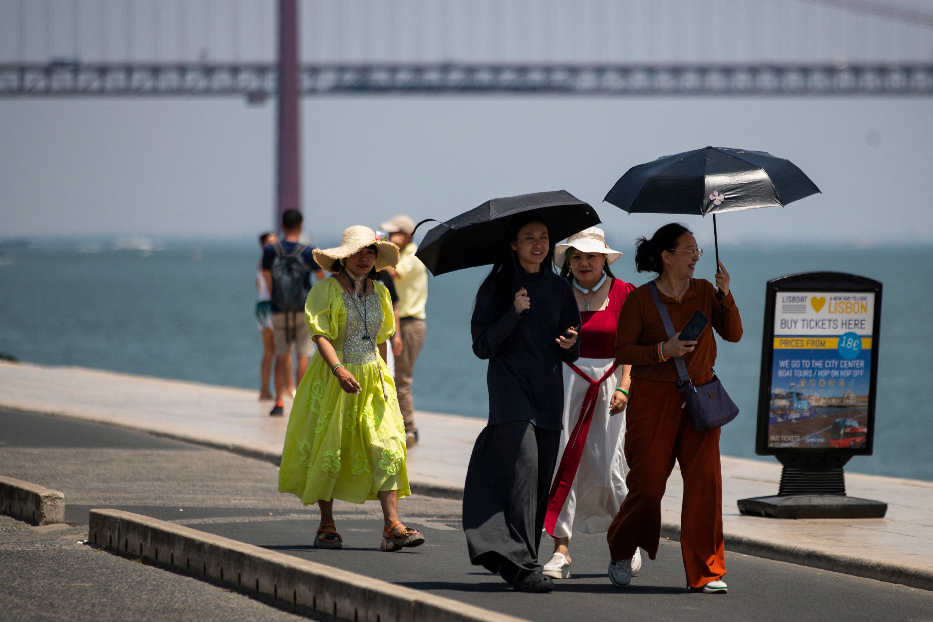 A group of women wear hats and hold umbrellas to shield themselves from the scorching sun during the first heatwave of the year in Lisbon, on June 29, 2025