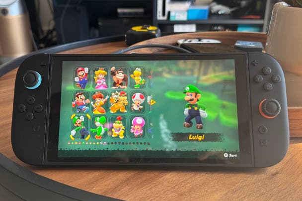 Original photography of the Nintendo Switch 2 in handheld mode showing the character select screen of Mario Kart World. The character Luigi is being selected