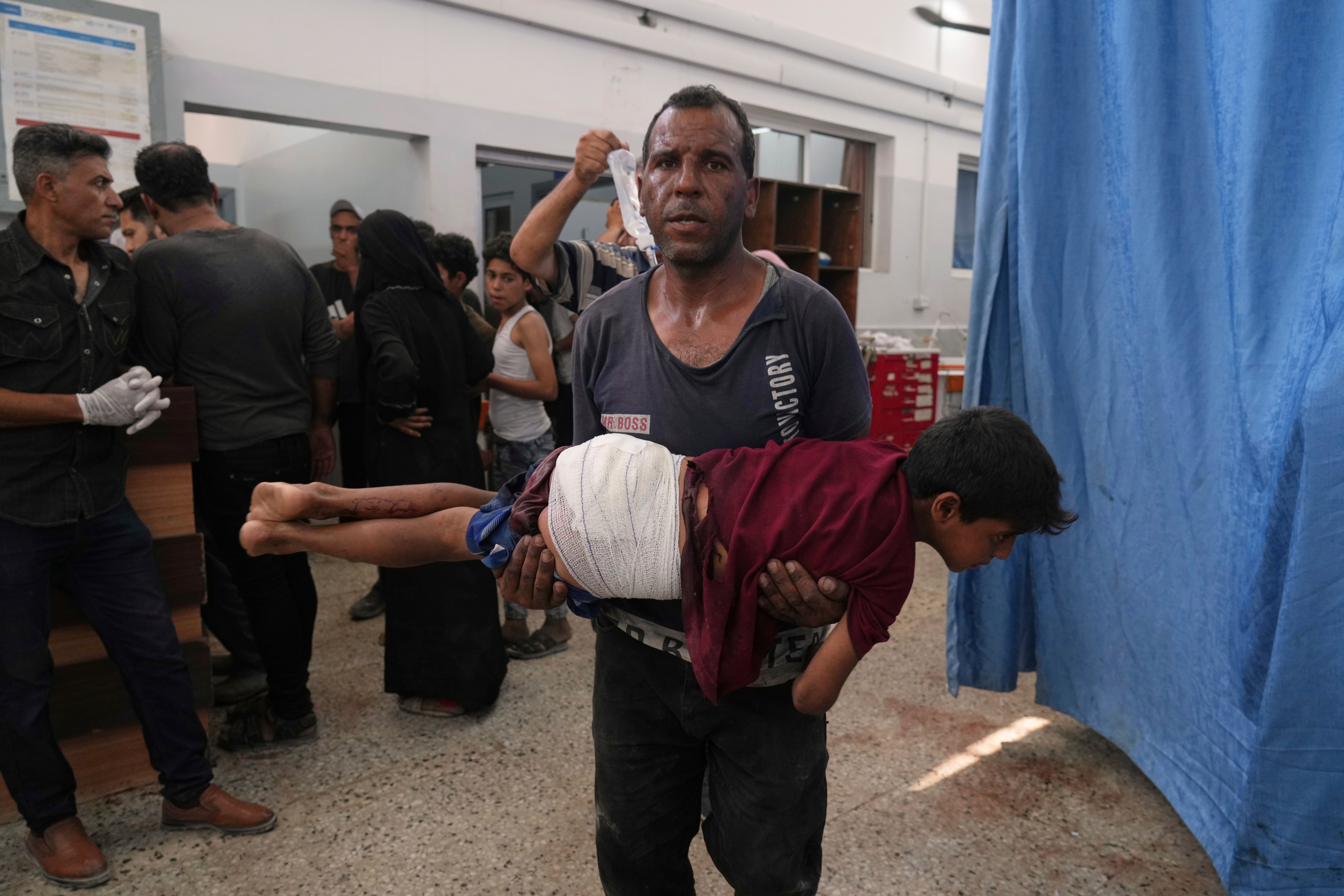 A man carries a child, who was wounded in an Israeli strike, after being treated in the Shifa Hospital, Gaza City, Monday, June 30