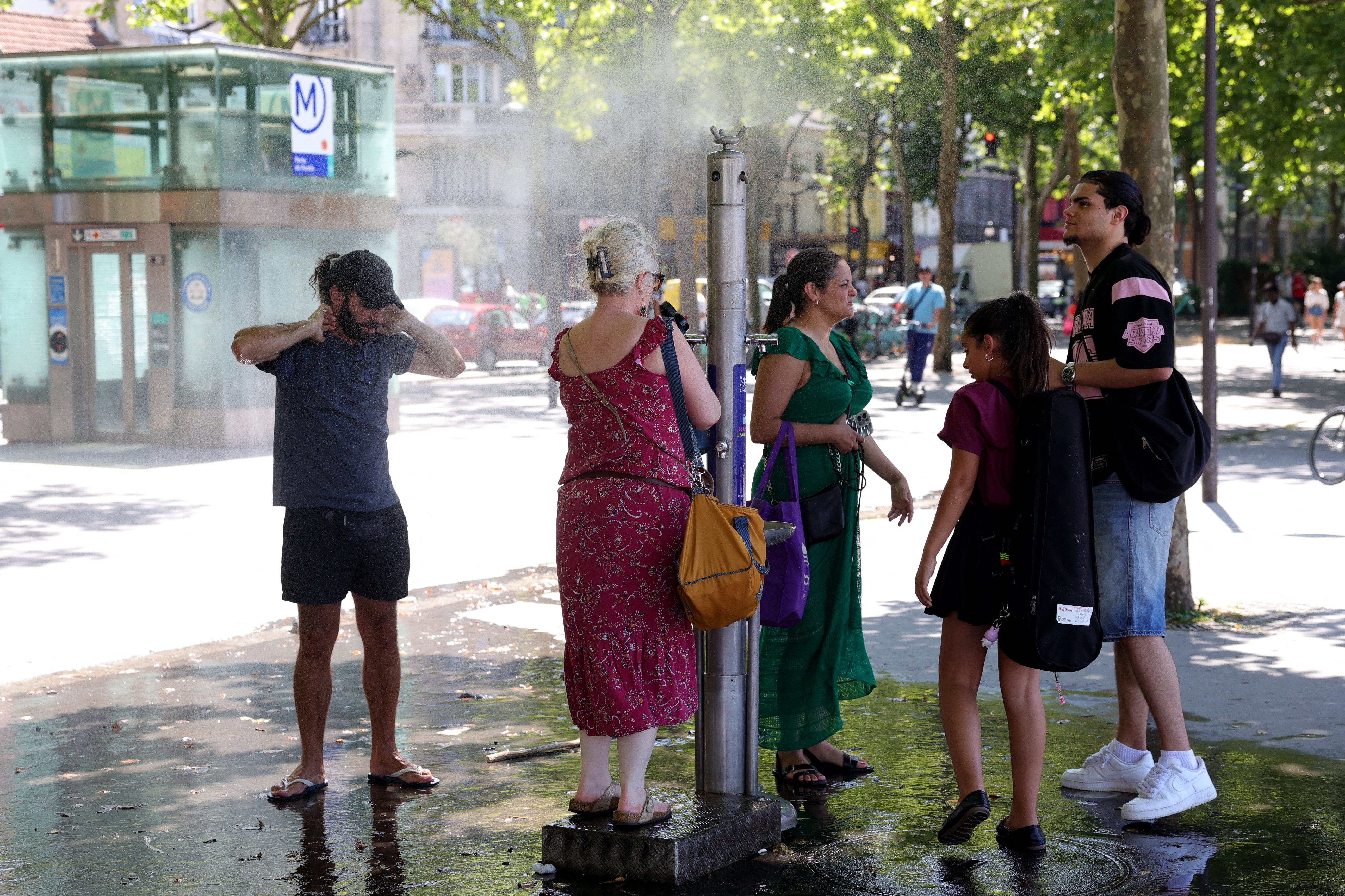 Pedestrians cool off with a public water jet in a street during a heatwave in Paris