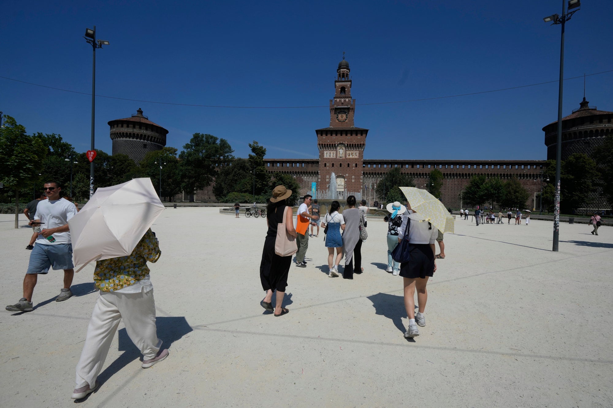 Tourists cover from the hot sun with umbrellas in front of the Sforzesco Castle, in Milan