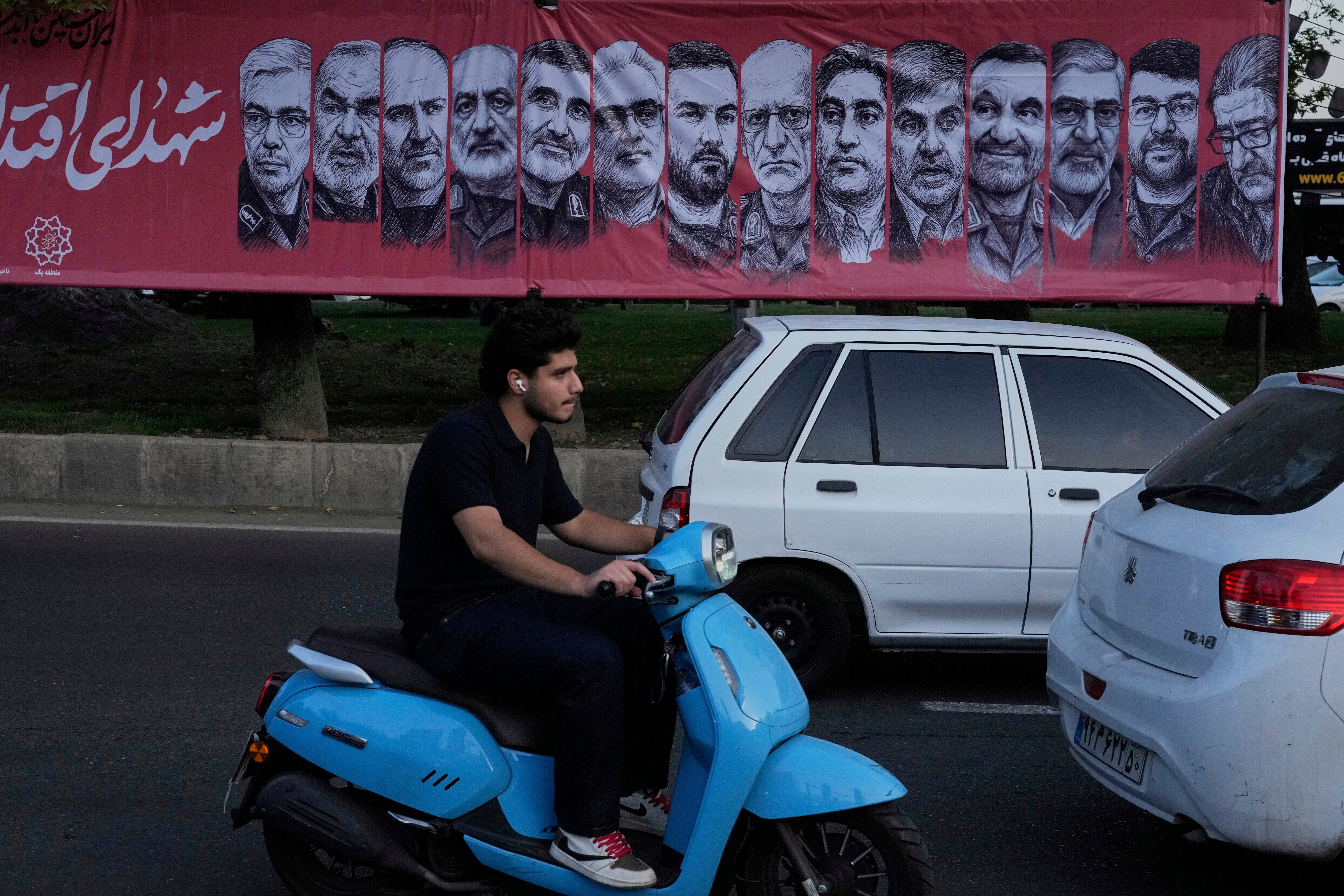 Vehicles drive past a banner showing portraits of the Iranian armed forces commanders and nuclear scientists who were killed in the Israeli strike