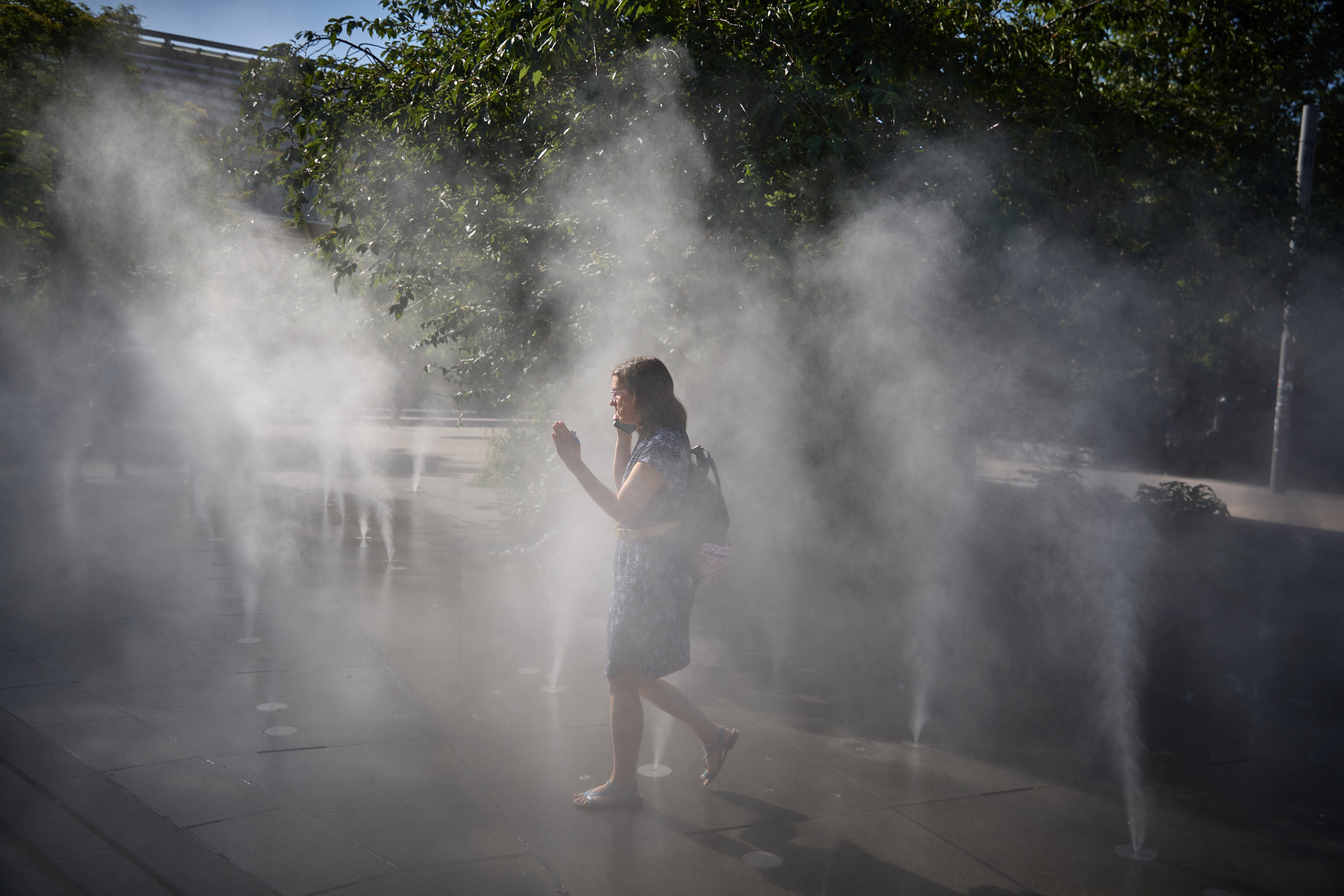 A woman walks through a mist fountain at a park in central Paris on Tuesday