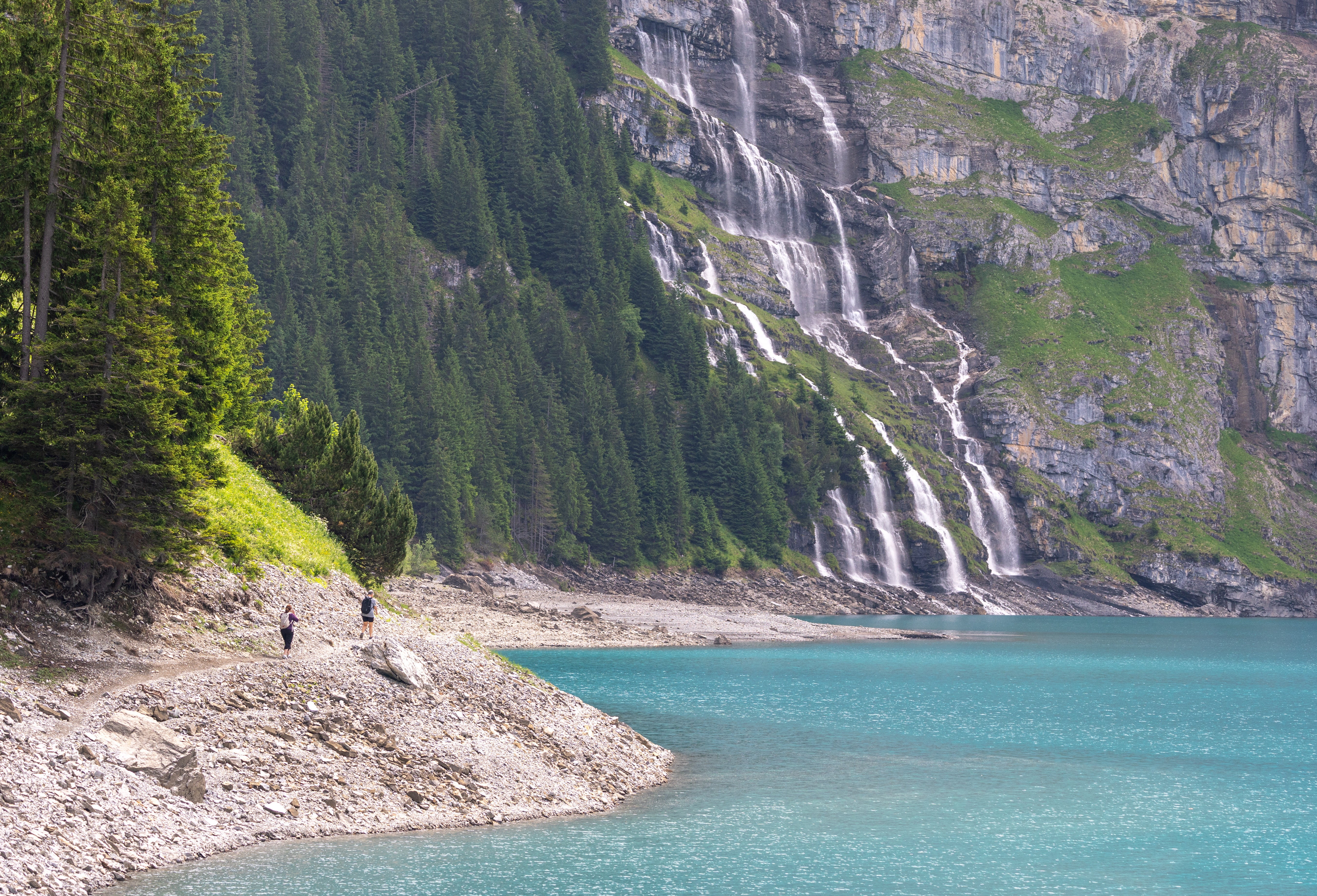 Hikers walk towards a waterfall at the Oeschinensee as rock falls from the Spitzen Stein threatens the village amid climate change and warming permafrost pose increasing challenges in Kandersteg, Switzerland, June 26, 2025