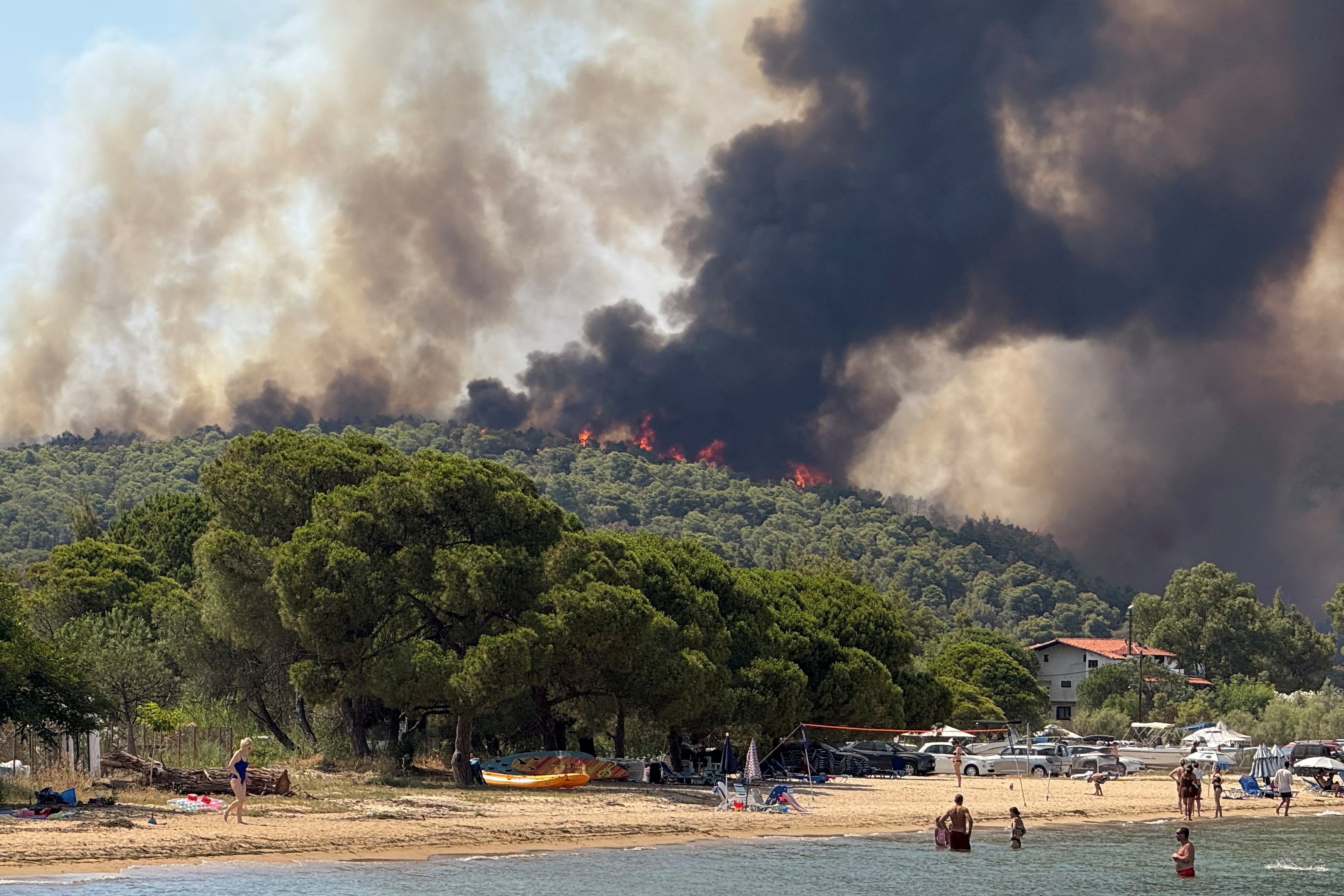 Beachgoers look at rising flames and smoke from a wildfire burning in Vourvourou village on Halkidiki peninsula, Greece, on 2 July 2025
