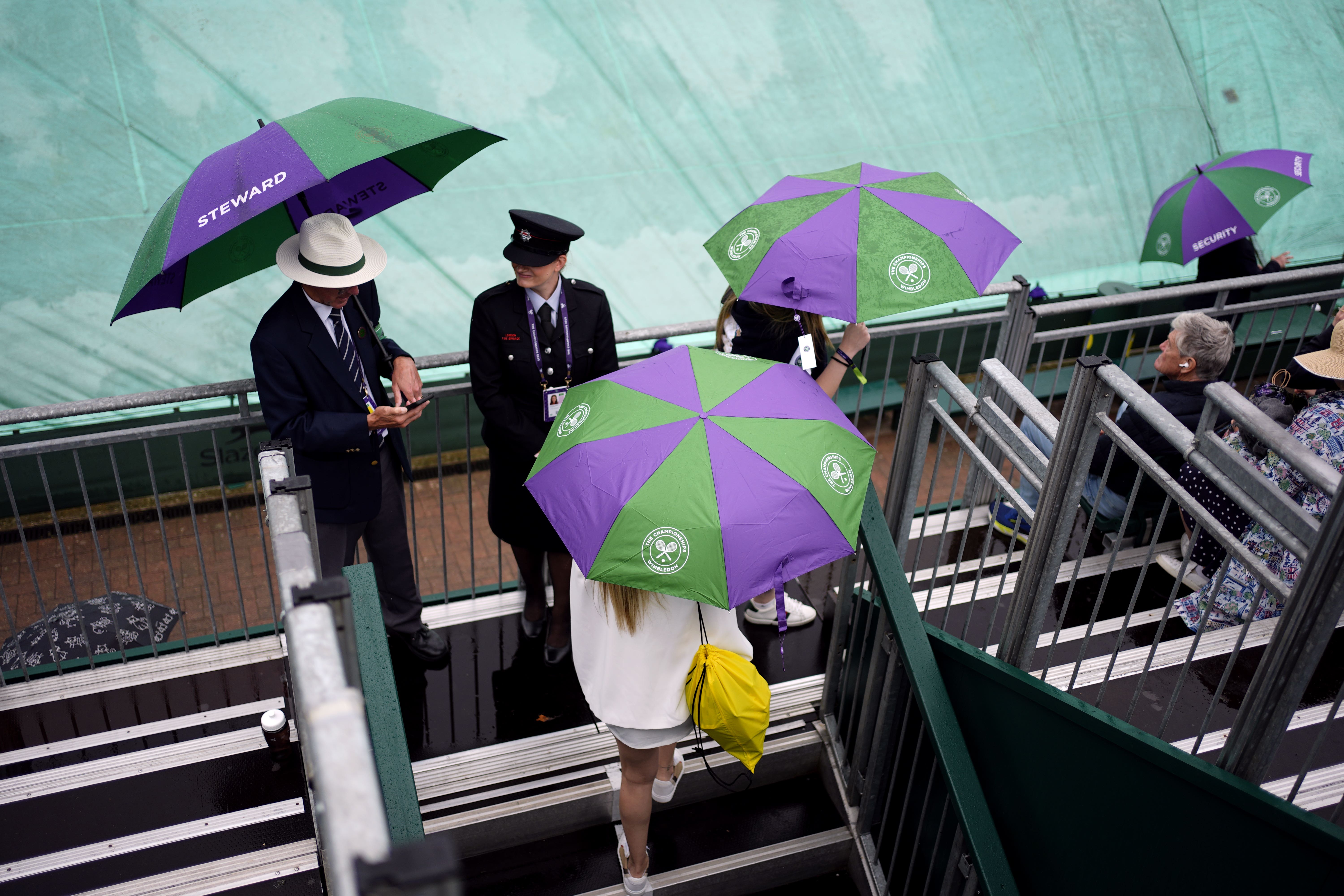 A spectator shelters from the rain on day three of the 2025 Wimbledon Championships (Jordan Pettitt/PA)
