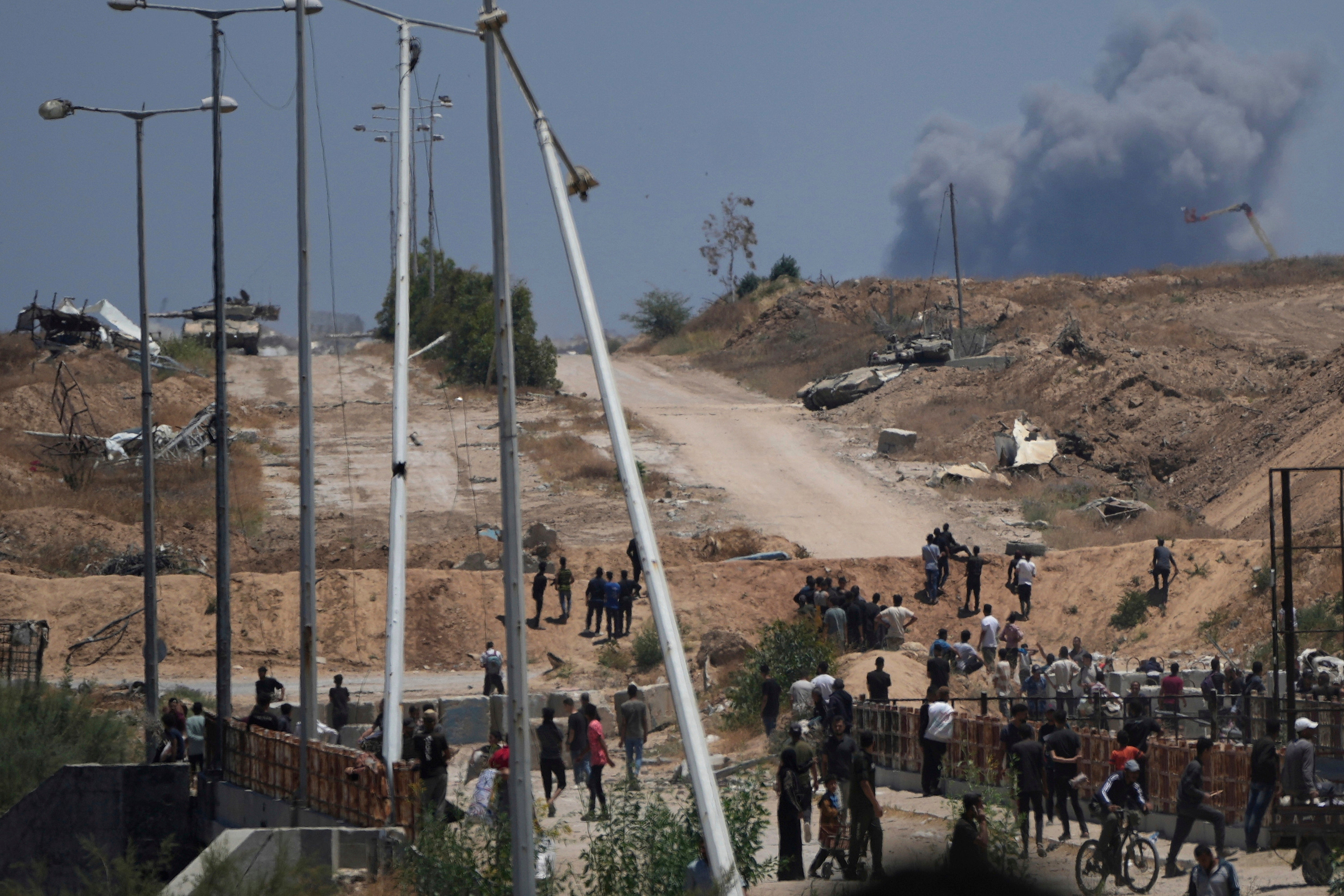Israeli army tanks are seen in the background as Palestinians gather at a GHF aid site