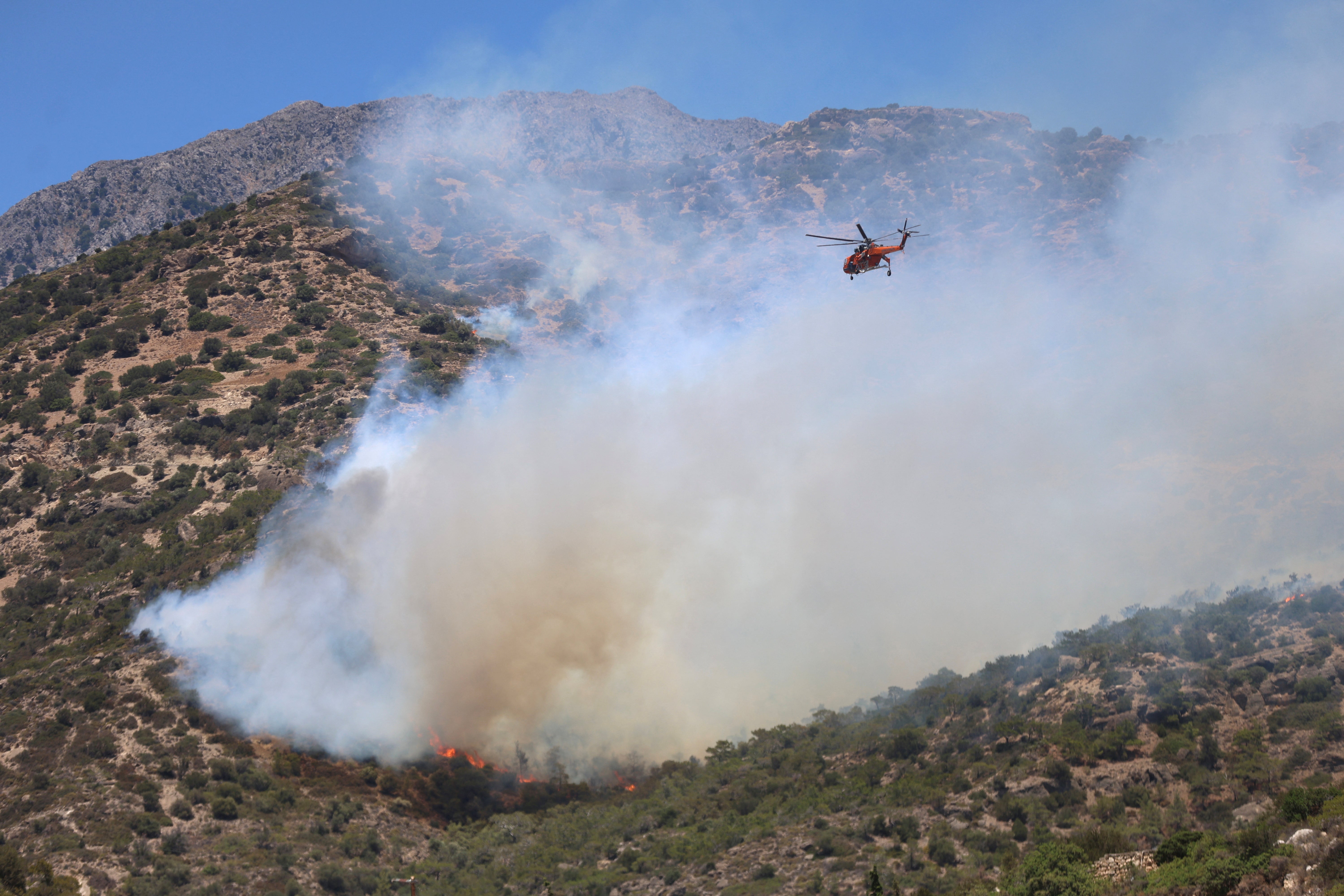 A firefighting helicopter flies near a wildfire burning near Ierapetra