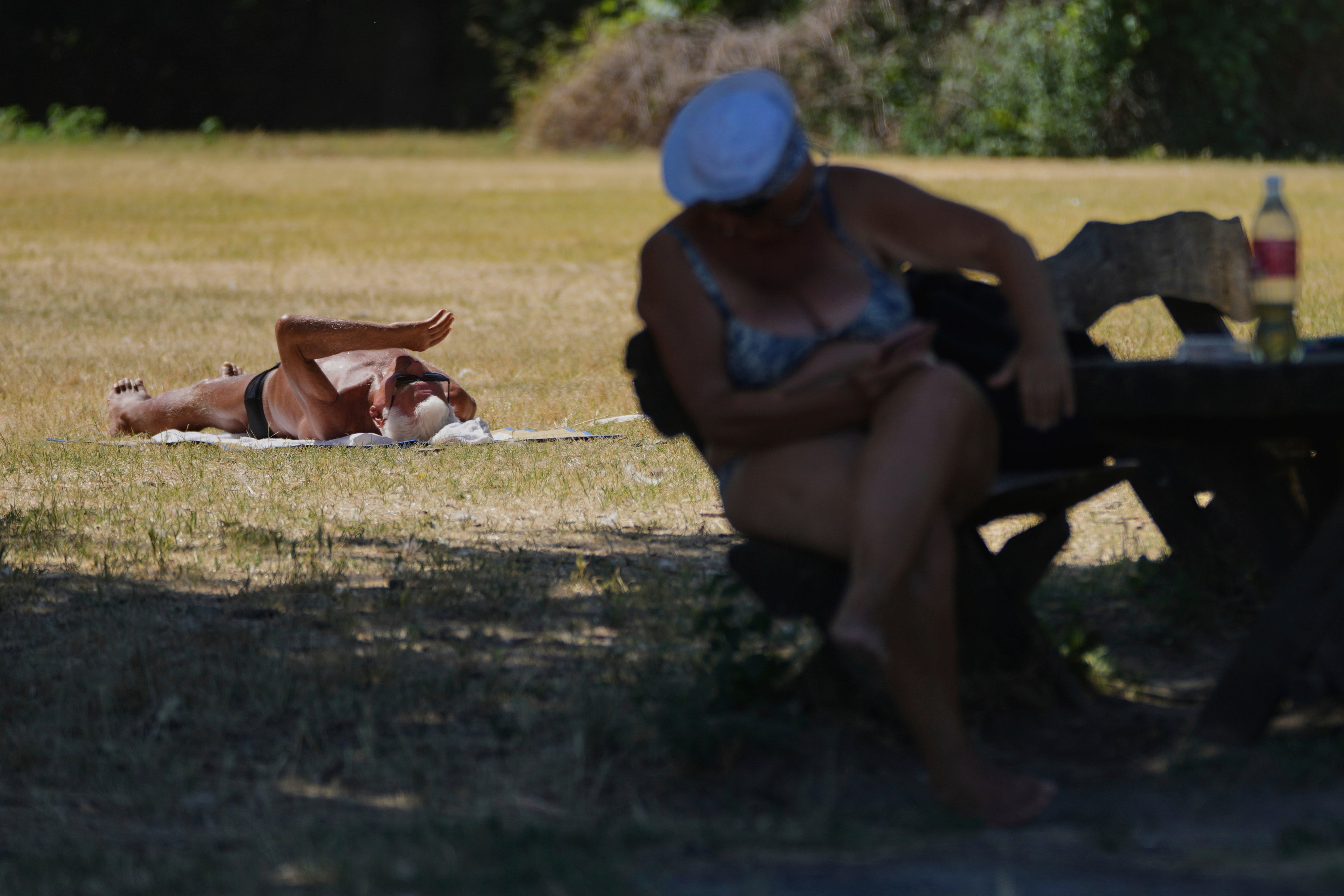 A person sits in the shade while another lies sunbathing during a hot summer day in Belgrade, Serbia