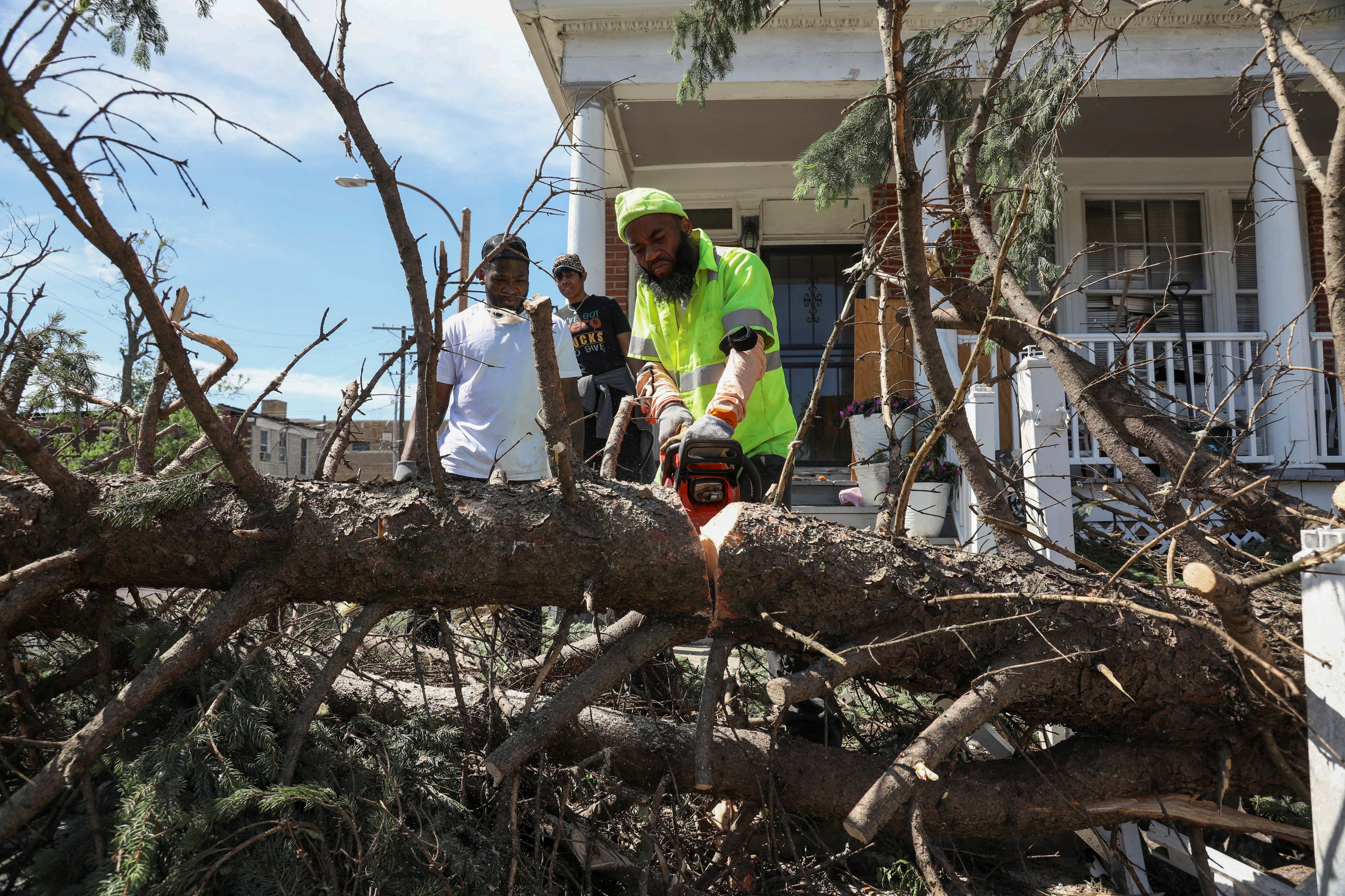A man uses a chainsaw to cut a fallen tree on the steps of a house after the tornado struck in St. Louis, Missouri