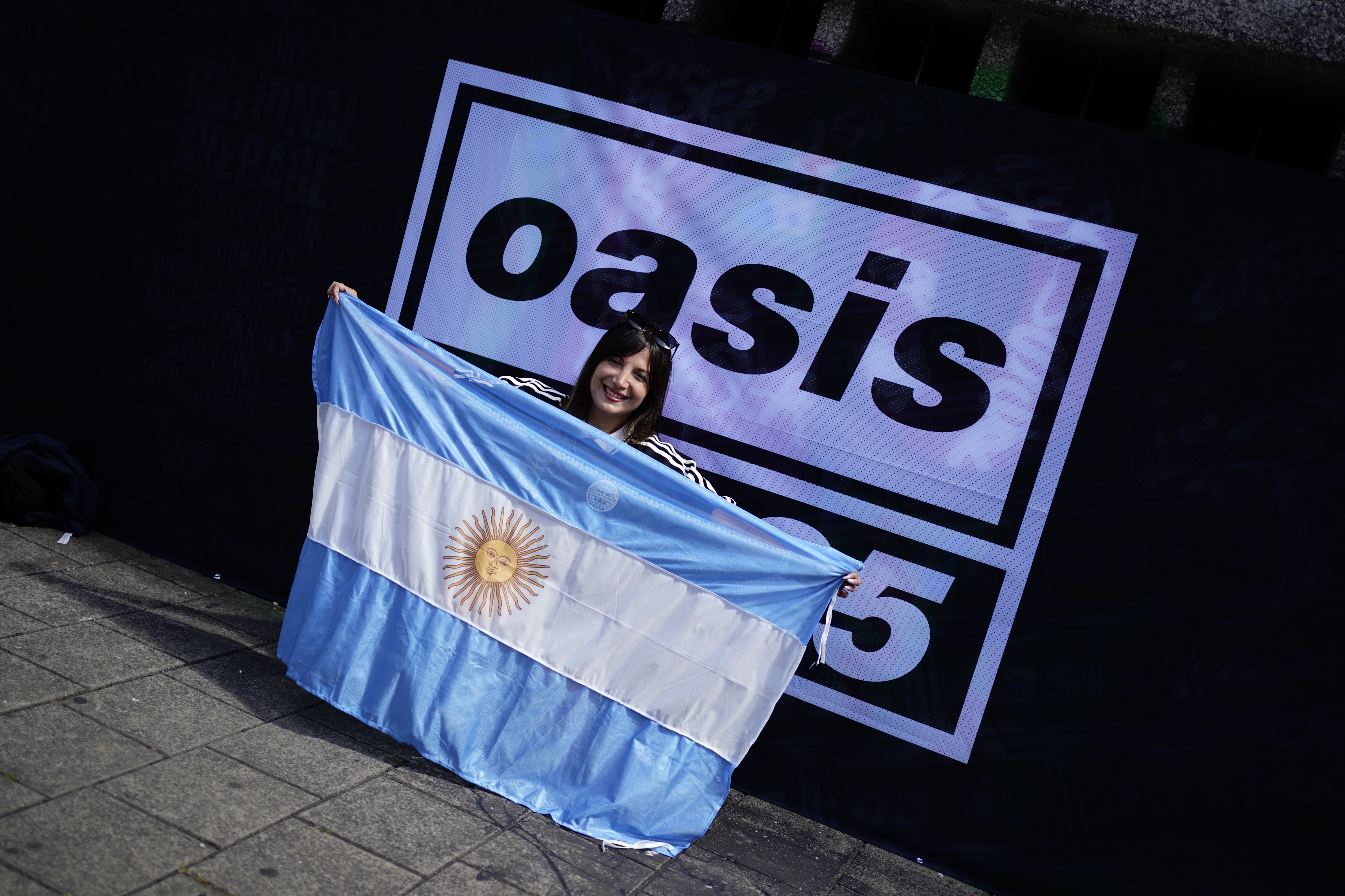 A fan from Argentina poses for a photo in front of an Oasis Live 25 sign (Jordan Pettitt/PA)