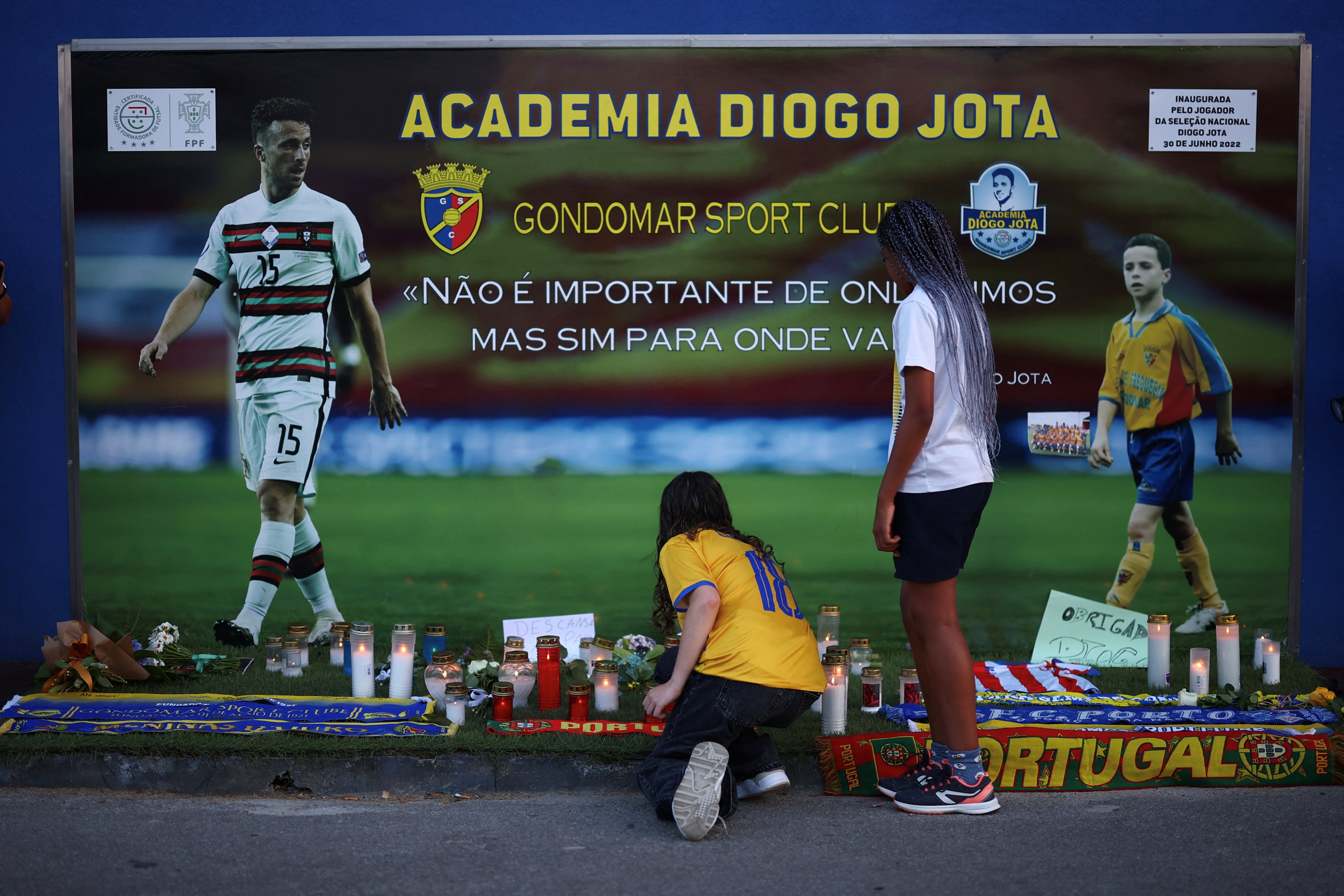A person kneels in front of a makeshift memorial for Portuguese footballer Diogo Jota at Academia Diogo Jota