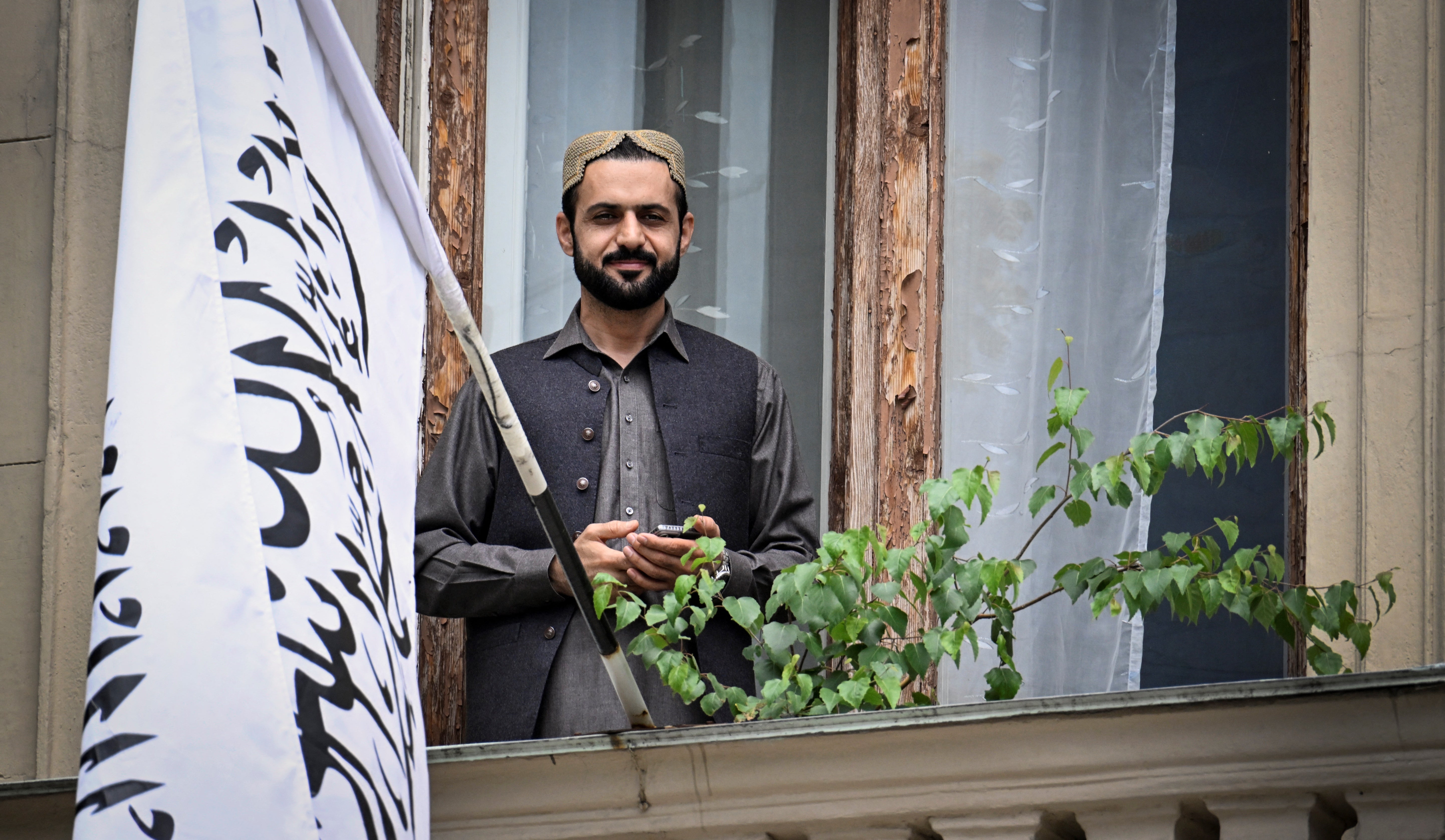 An official stands next to the flag of the Islamic Emirate of Afghanistan on the balcony of the Afghan embassy in Moscow