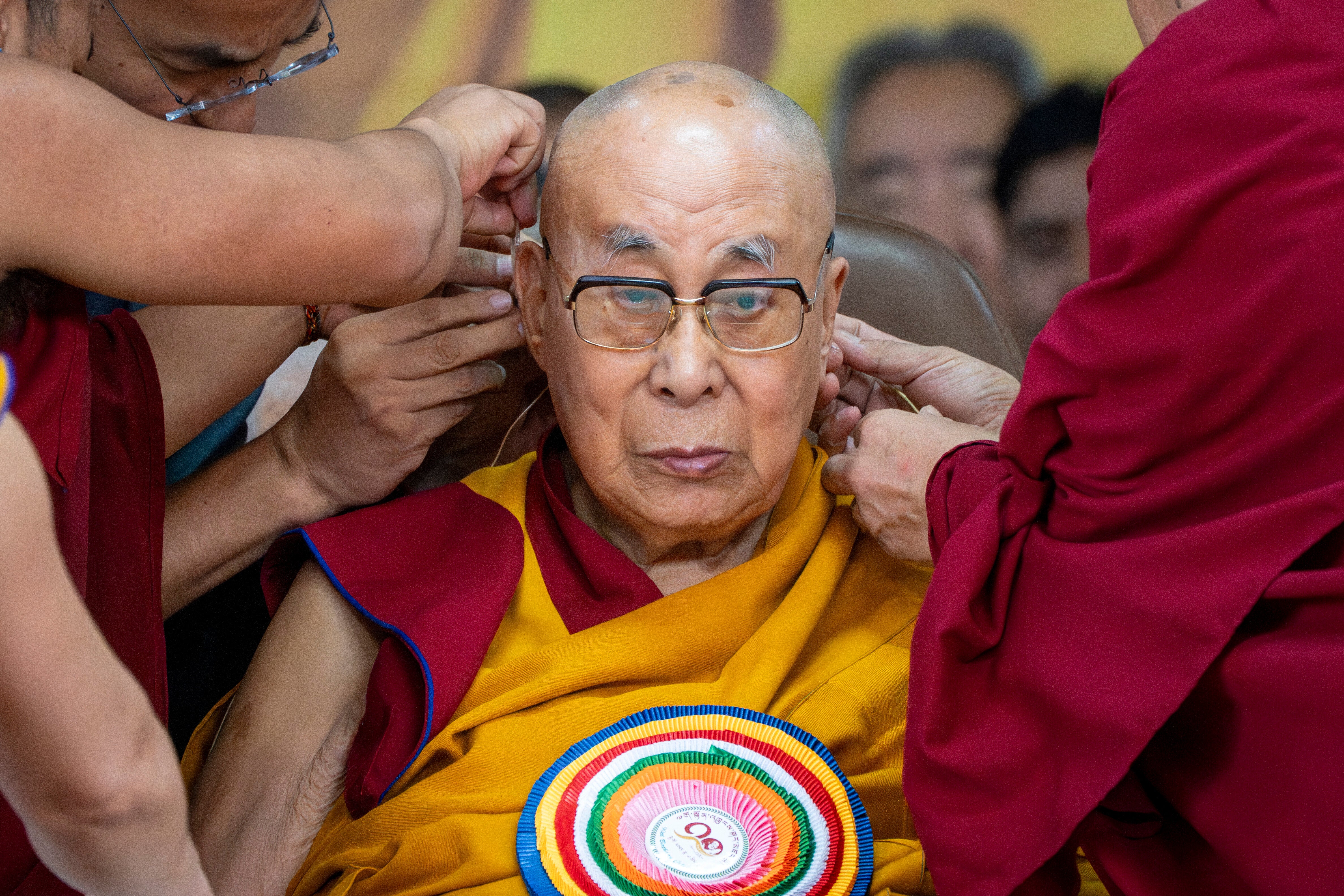 Attendant monks help put a microphone around Tibetan spiritual leader the Dalai Lama's head during his 90th birthday celebrations at the Tsuglagkhang temple in Dharamshala