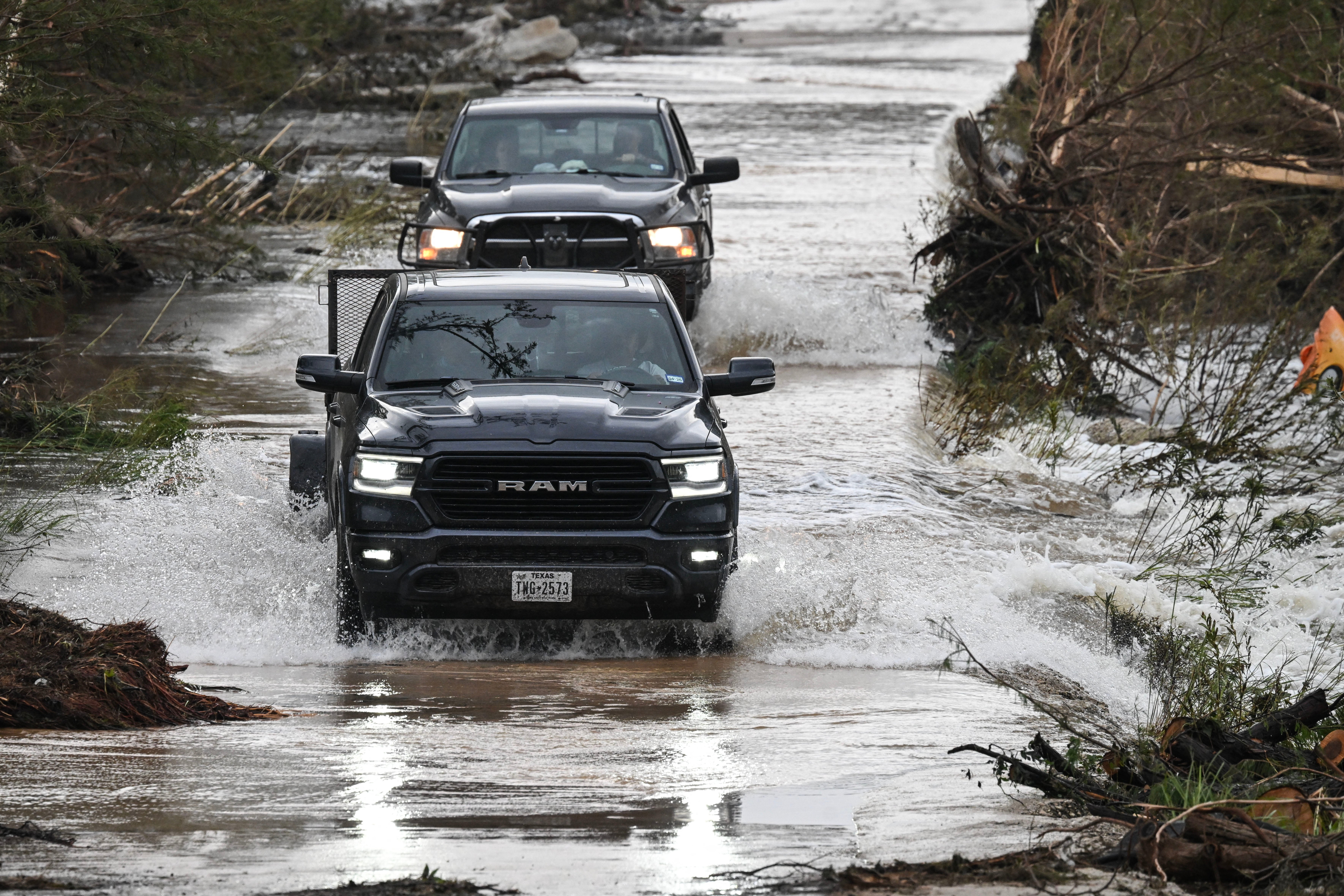 Trucks drive through a flooded and damaged road in Hunt, Texas, days after severe flash floods destroyed camps and homes along the Guadalupe River