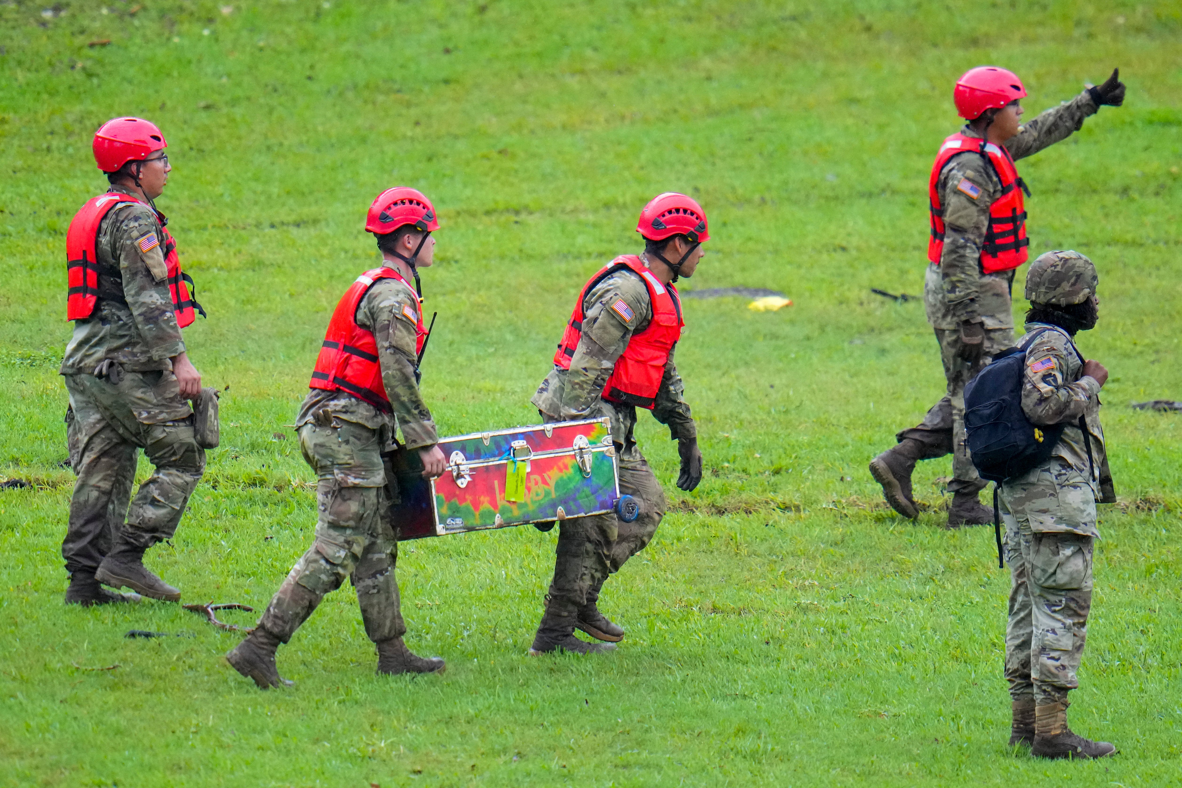 The search for missing people has entered its fourth day after 82 total deaths from the floods have been confirmed. Military personnel carry a camp trunk salvaged downriver from Camp Mystic.
