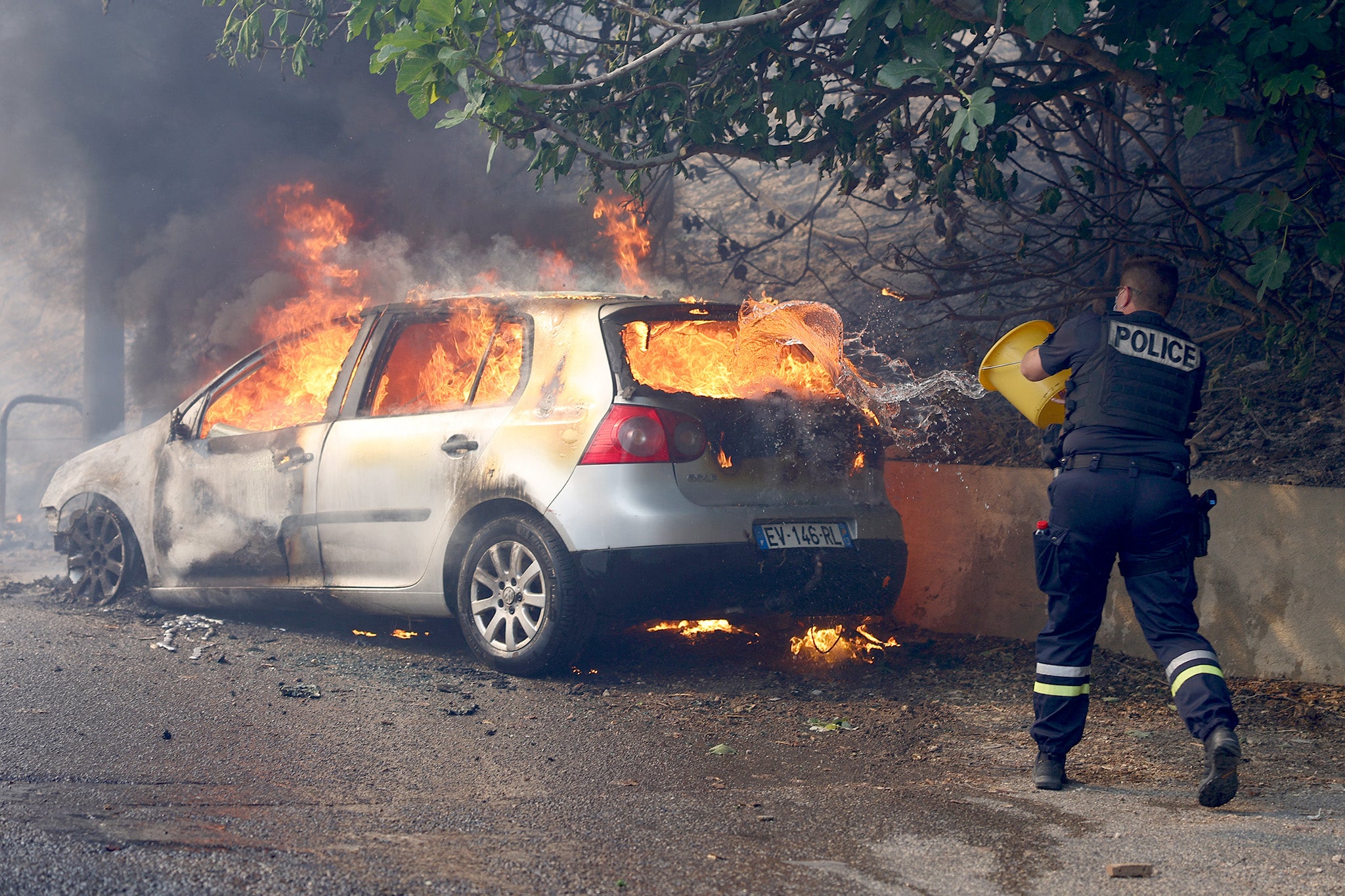 A police officer tries to put off the fire in a car during a wildfire, in L'Estaque district of Marseille, southern France on 8 July