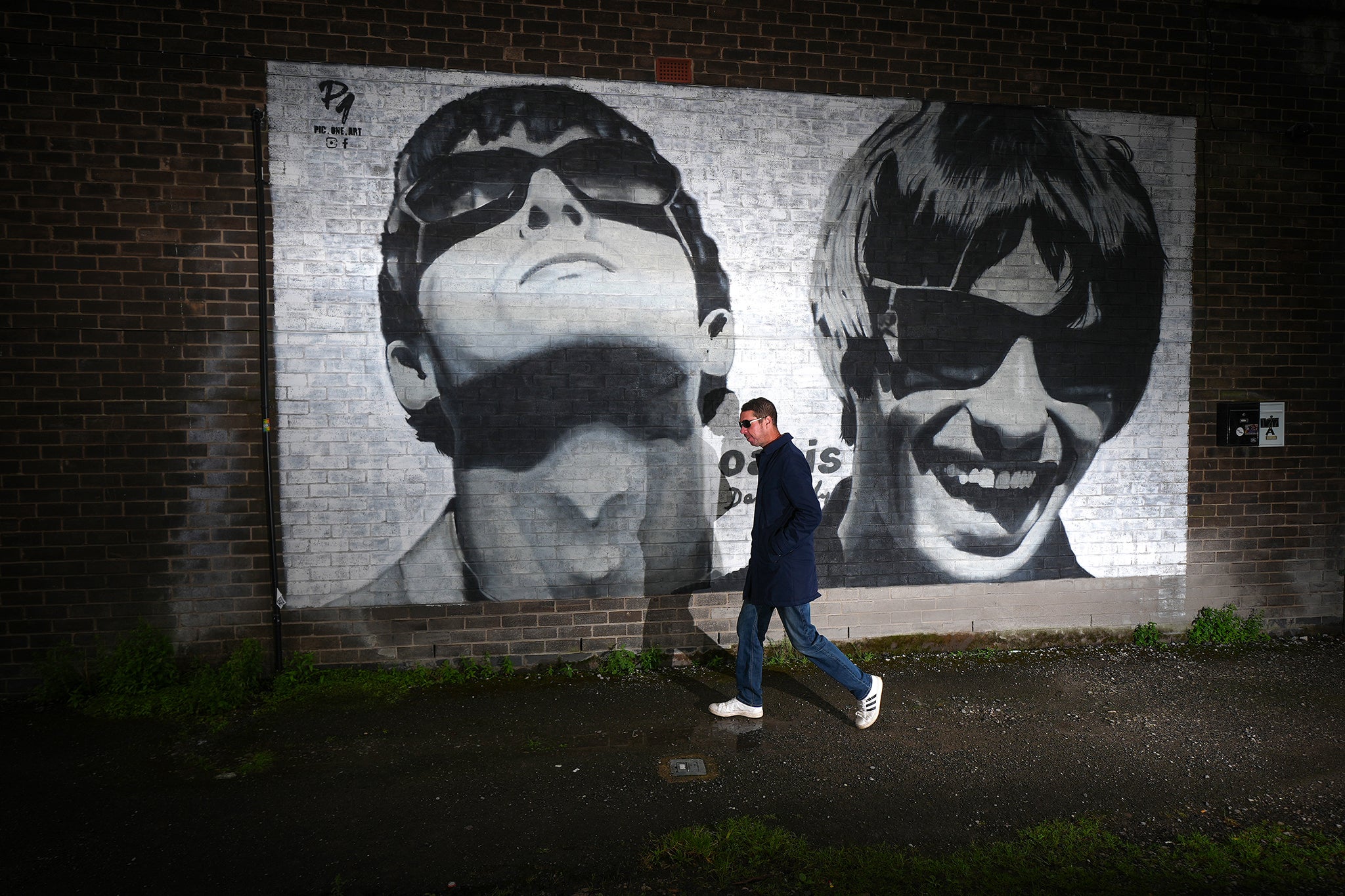 An Oasis fan is photographed next to a new mural depicting Liam and Noel Gallagher of Oasis