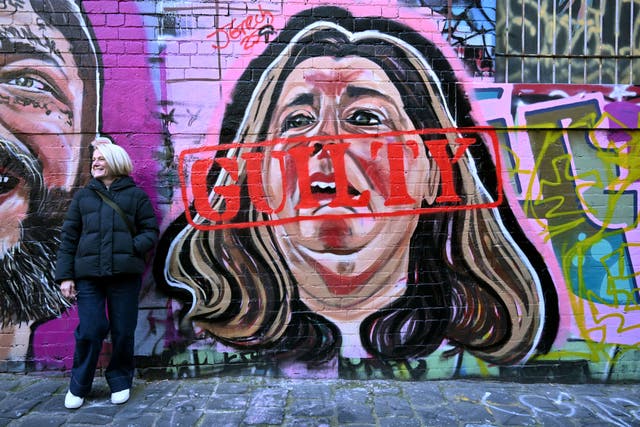 <p>File. A woman poses by a mural by street artist Jarrod Grech of Erin Patterson - now stamped with a guilty sign - of the Australian woman found guilty of murdering three members of her husband’s family with a toxic mushroom-laced beef Wellington lunch</p>