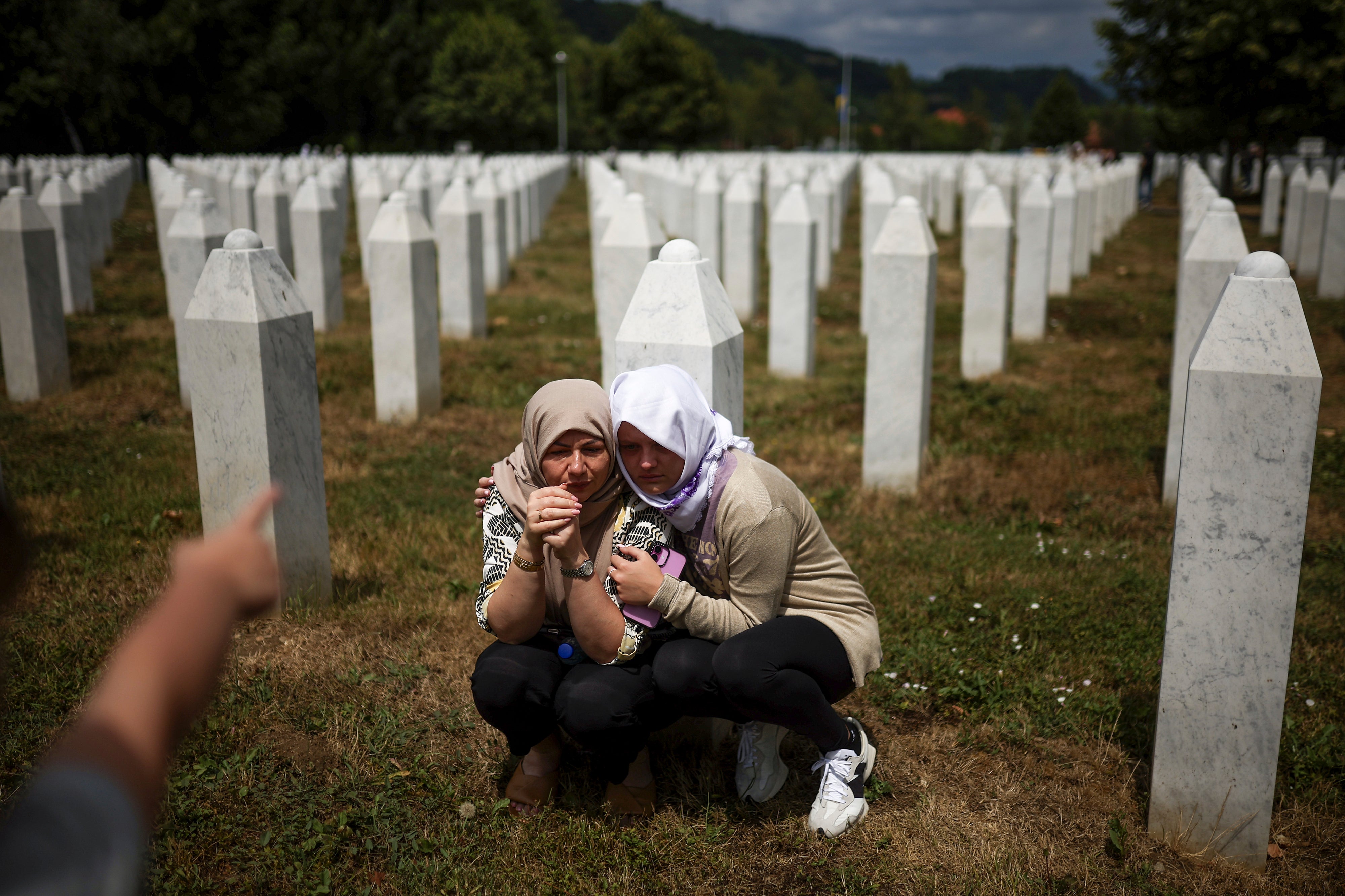 Family members mourn next to the grave of their relative, a victim of the Srebrenica genocide