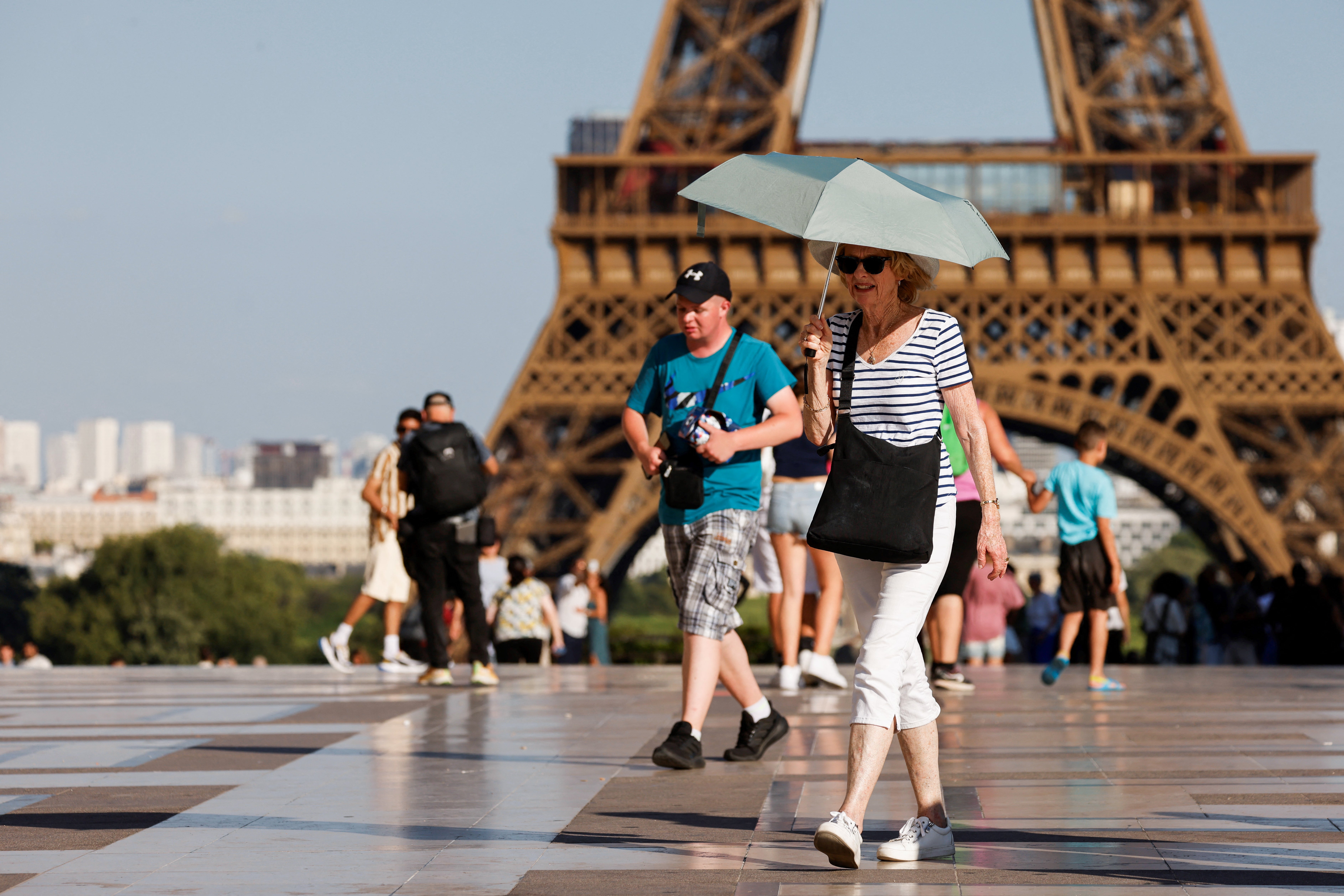 A tourist uses an umbrella to protect herself from the sun outside the Eiffel Tower